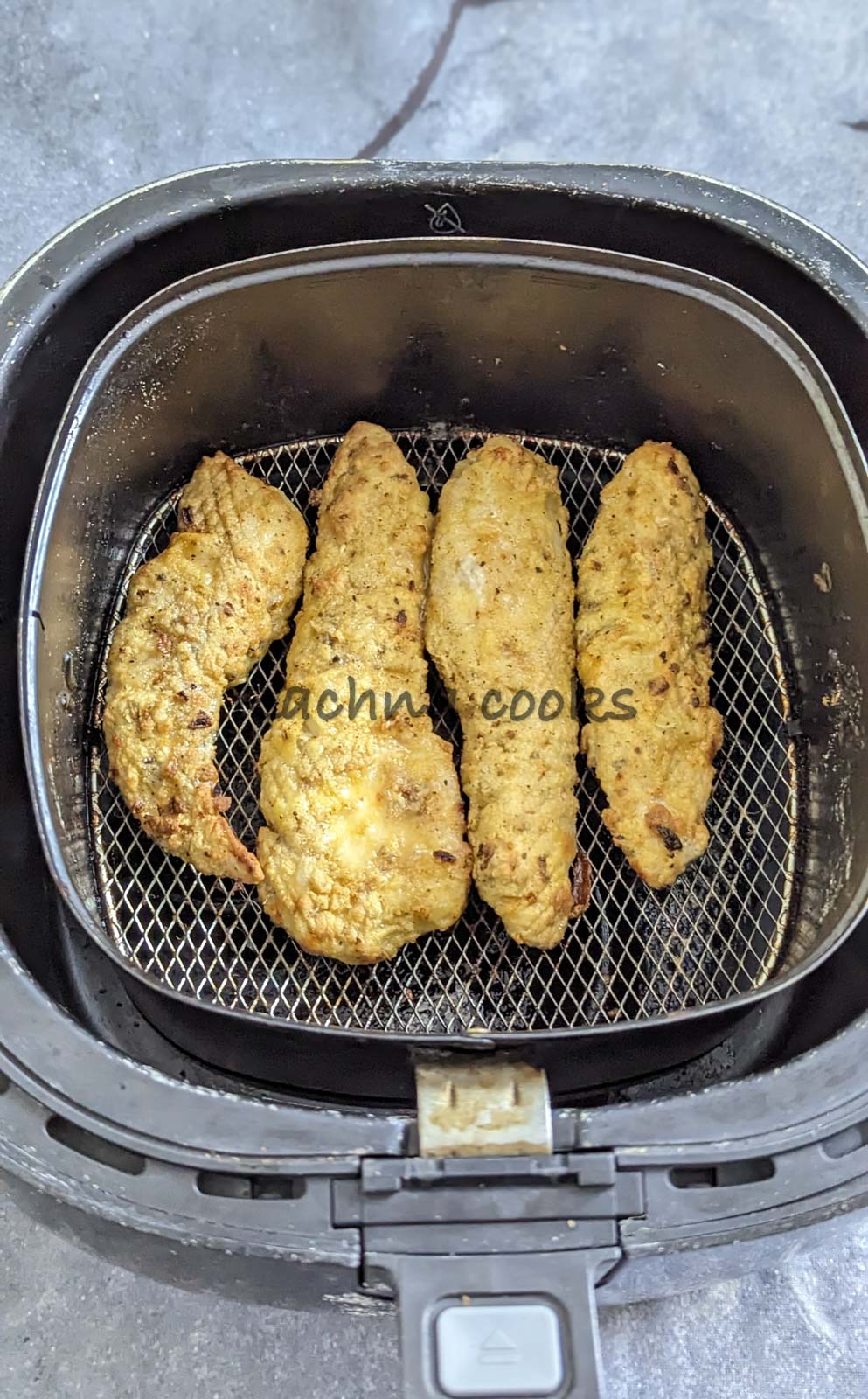 4 crispy cooked chicken tenders in air fryer basket.
