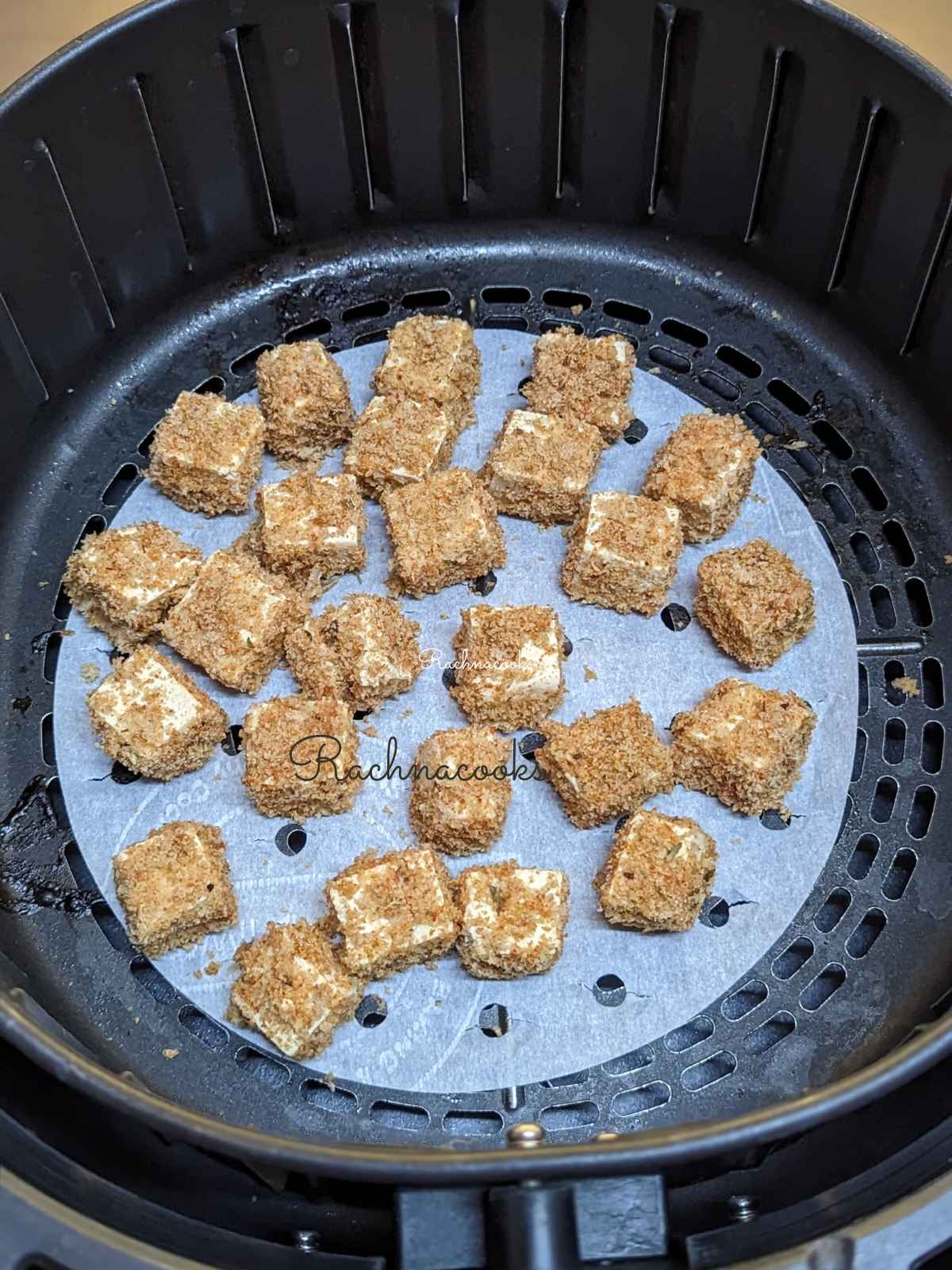 Air fryer crispy tofu placed on top of perforated parchment paper in air fryer