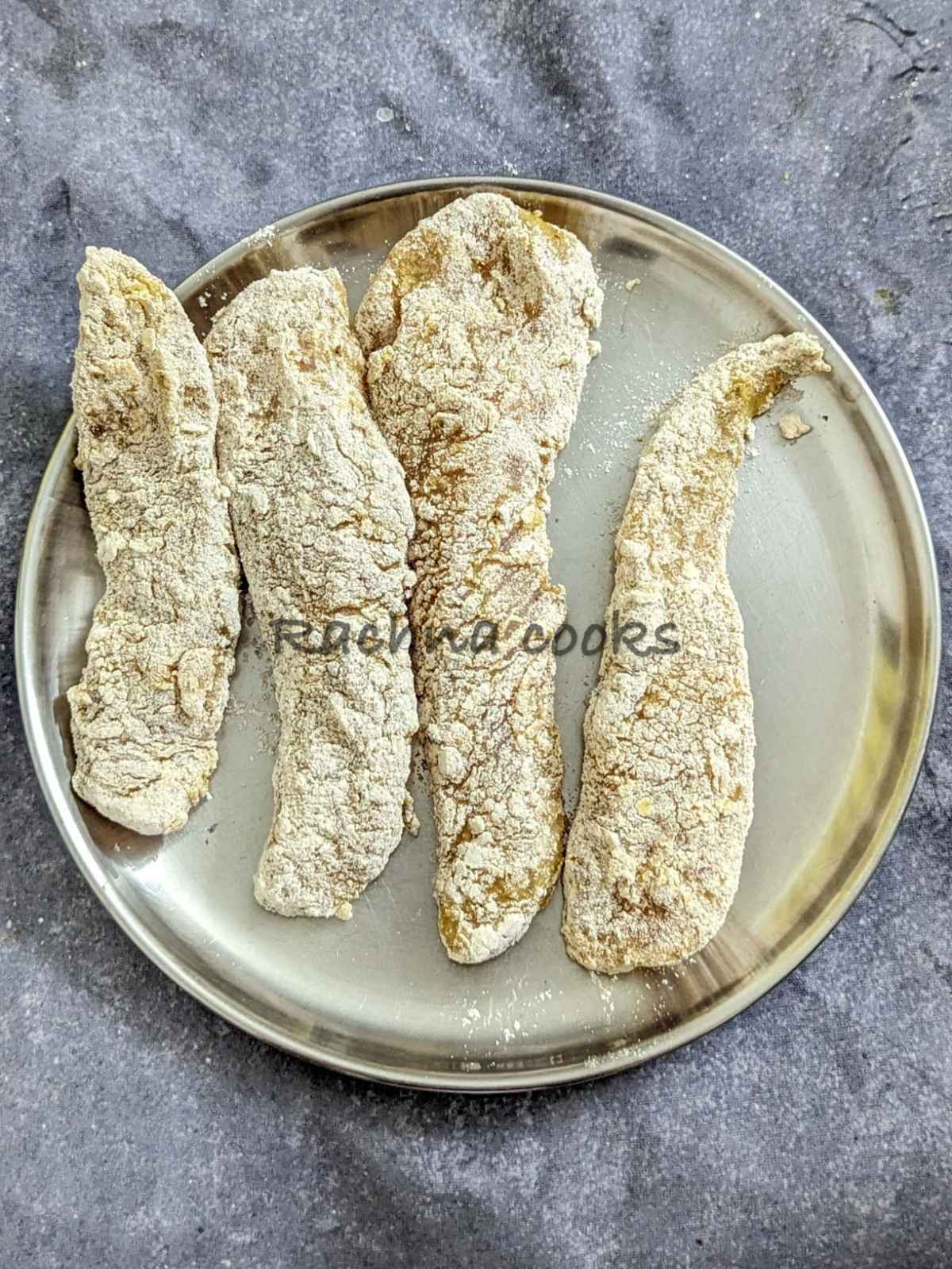4 chicken tenders after breading on a plate.