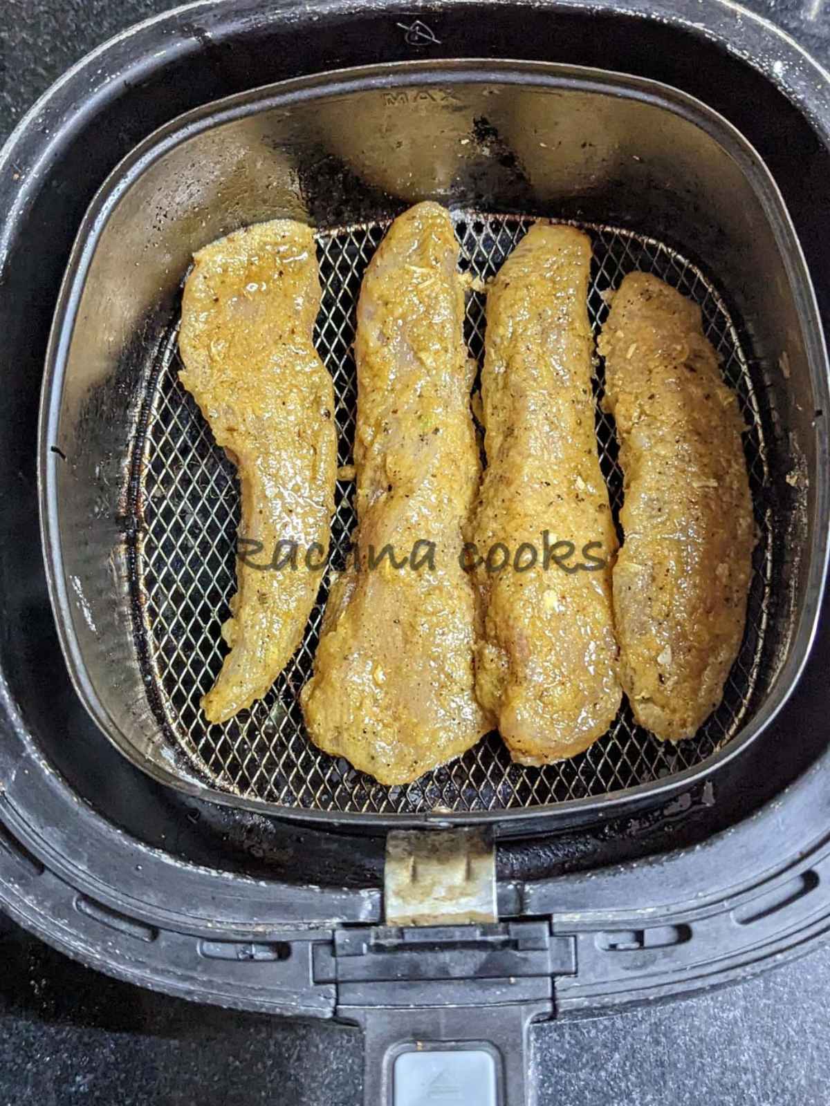 4 breaded chicken tenders in air fryer basket after spraying with olive oil