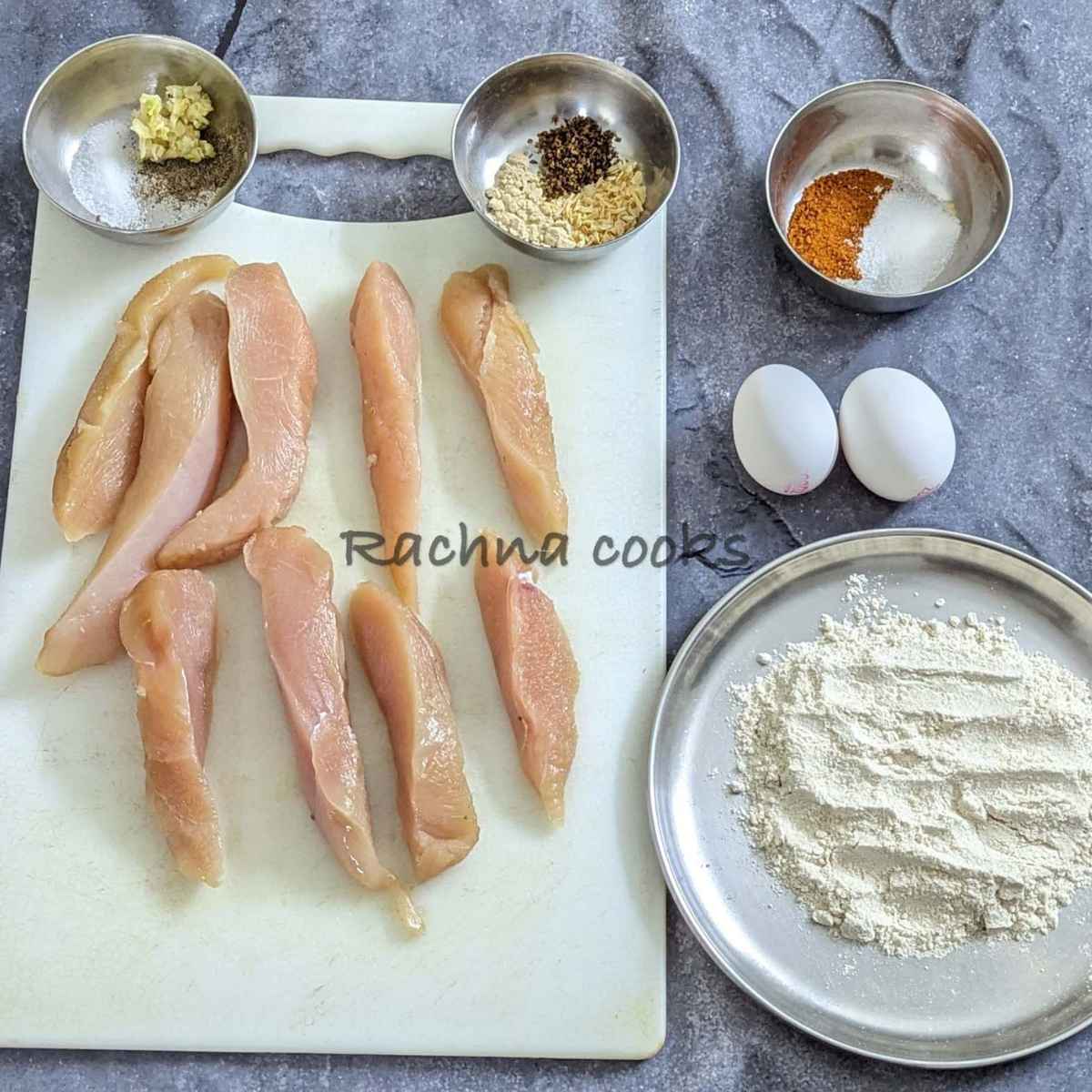 The ingredients for Buffalo chicken tenders laid out: chicken tenders, seasonings for chicken and breading, eggs and flour.