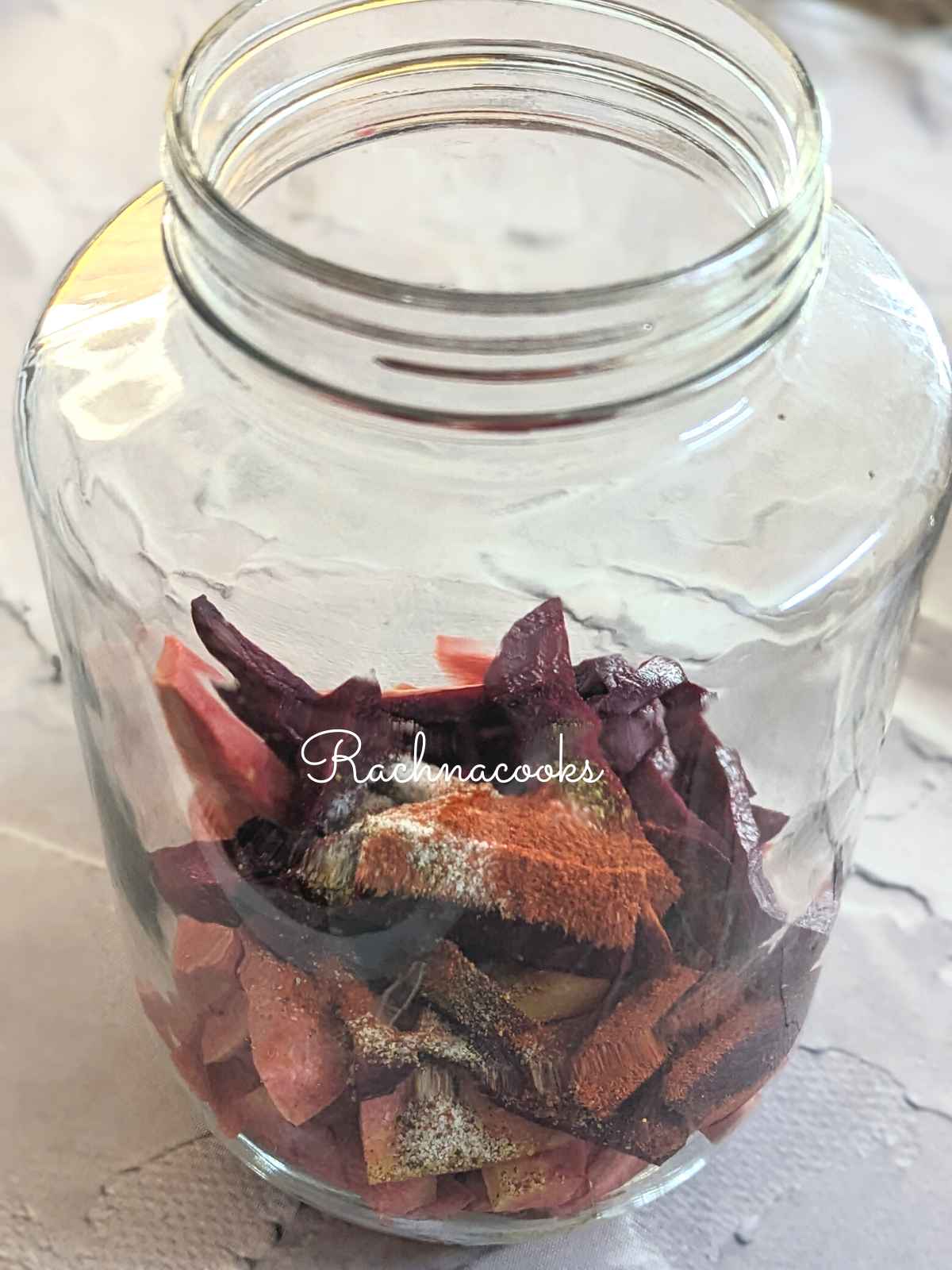 A glass jar with carrot and beet batons, mustard powder, cayenne, salt and black salt.