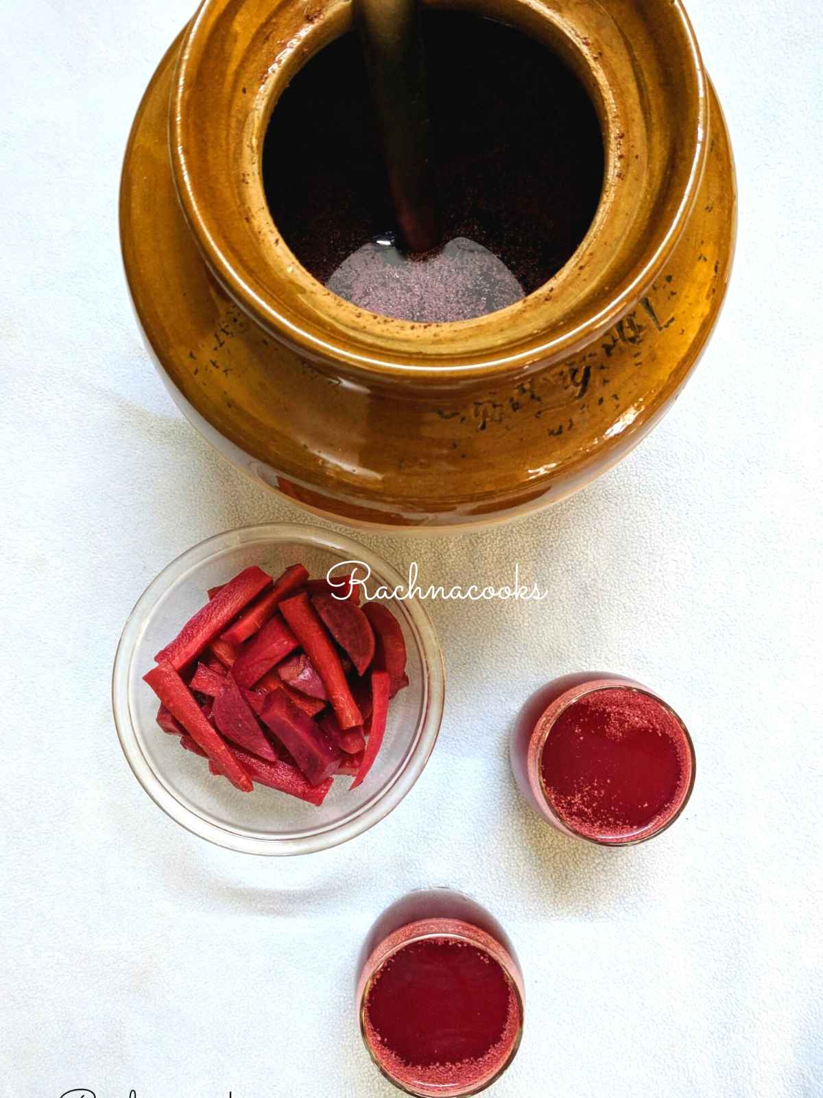 Top shot of kanji in a ceramic bowl with 2 glasses of kanji and carrot and beet batons in a glass bowl.