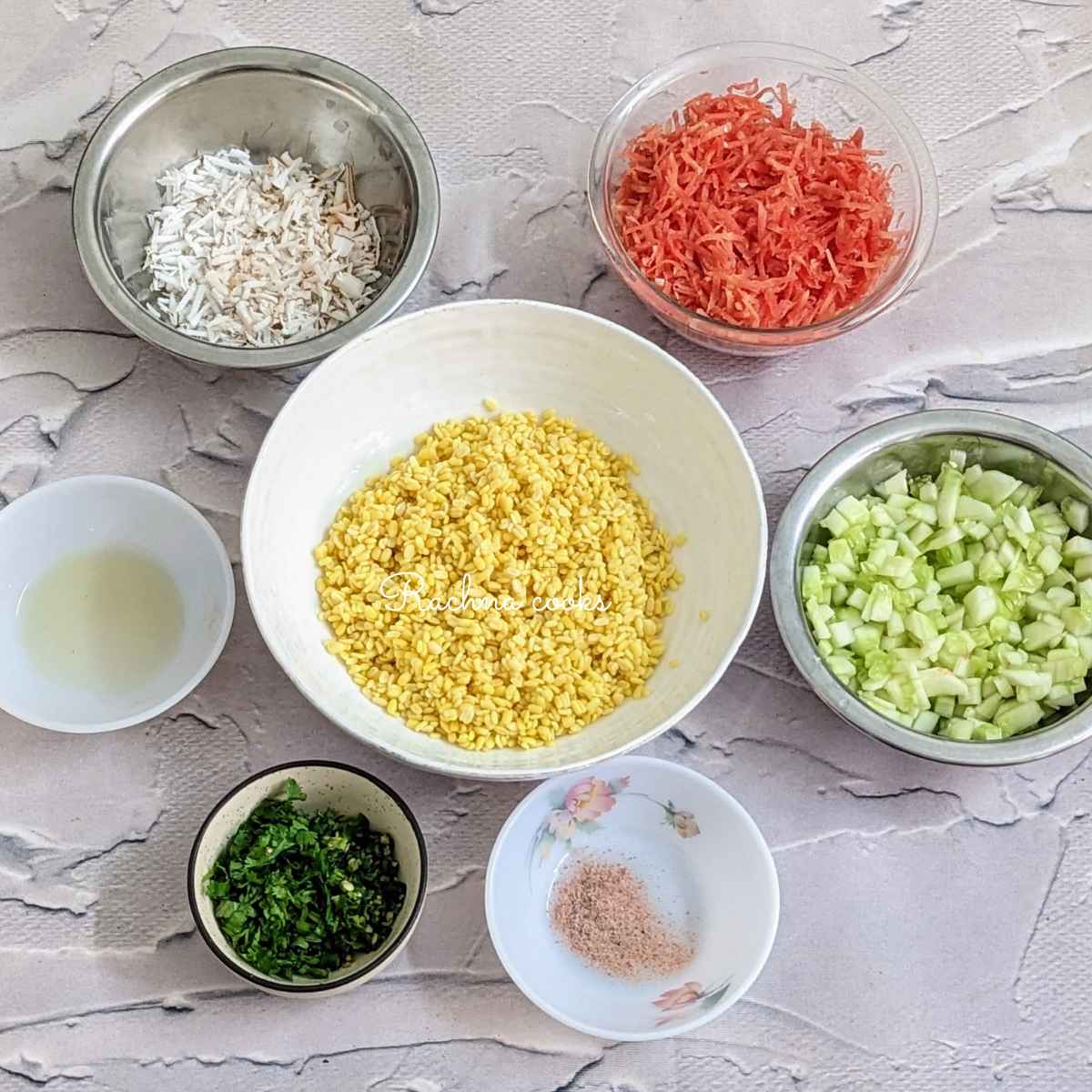 Soaked and drained moong dal, lemon juice, salt, chopped cucumber, grated carrot, grated coconut, chopped cilantro and green chilli in different bowls.