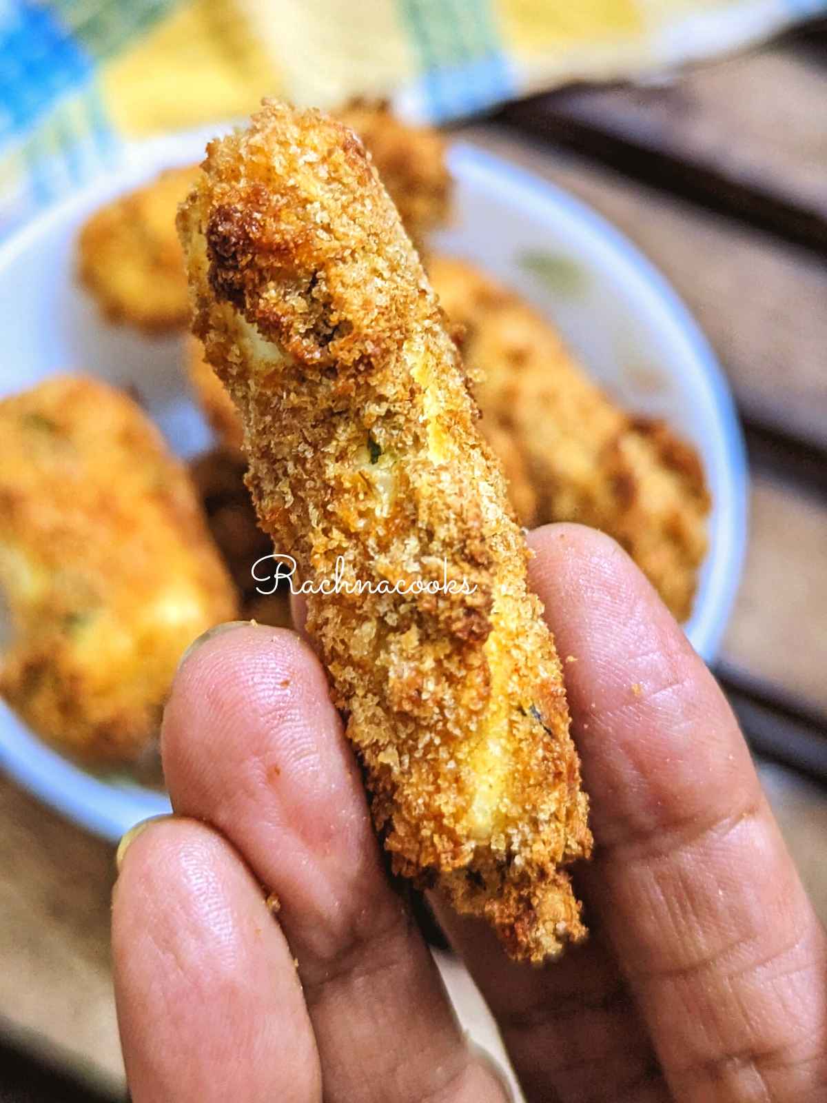 1 crispy air fried paneer finger held up in hand.