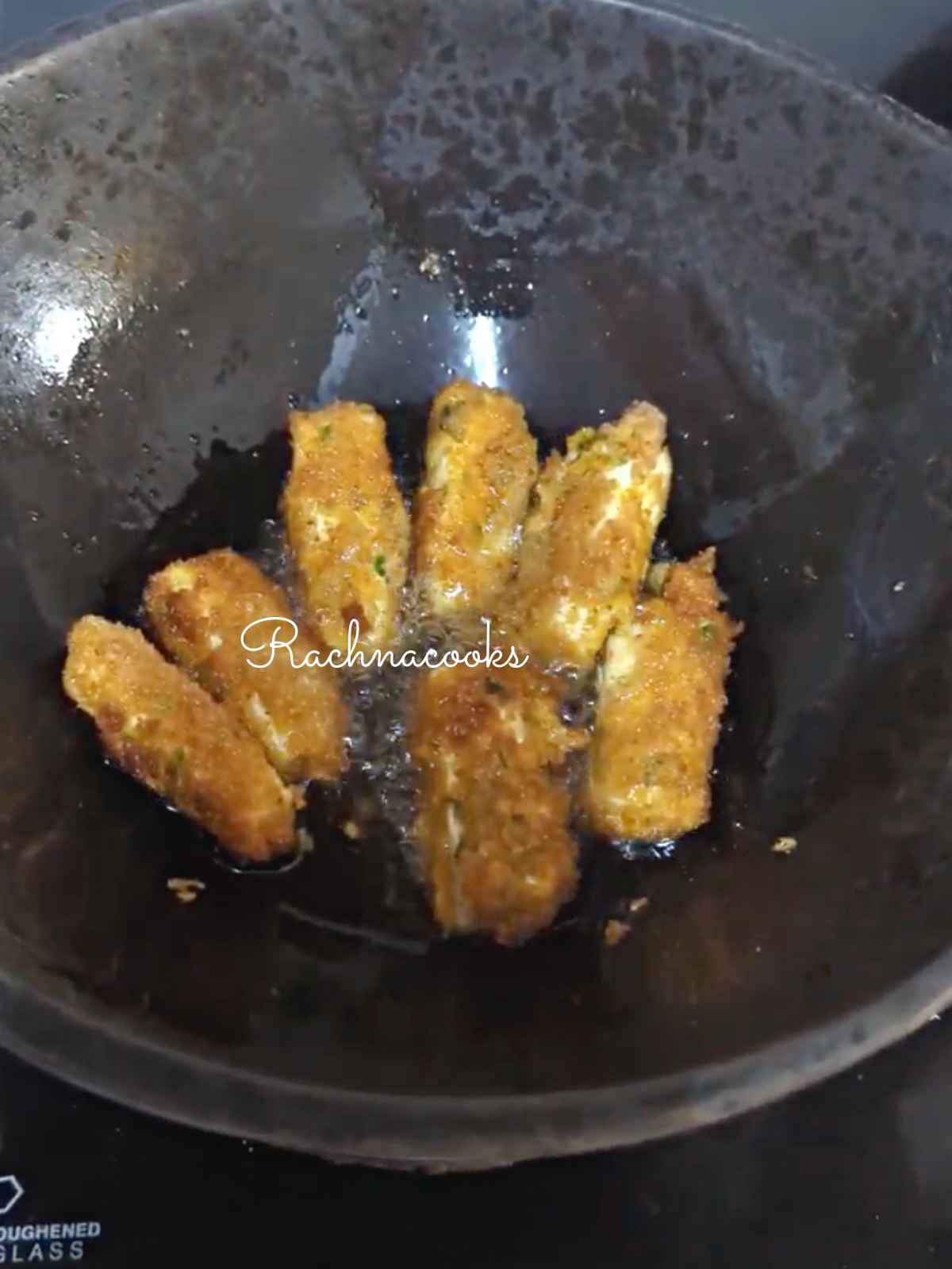 paneer fingers being deep fried in oil in a wok.