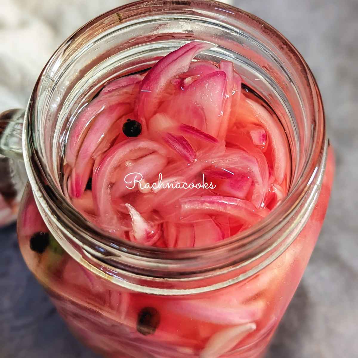 Pink pickled sliced onion in a mason jar in pickling solution.