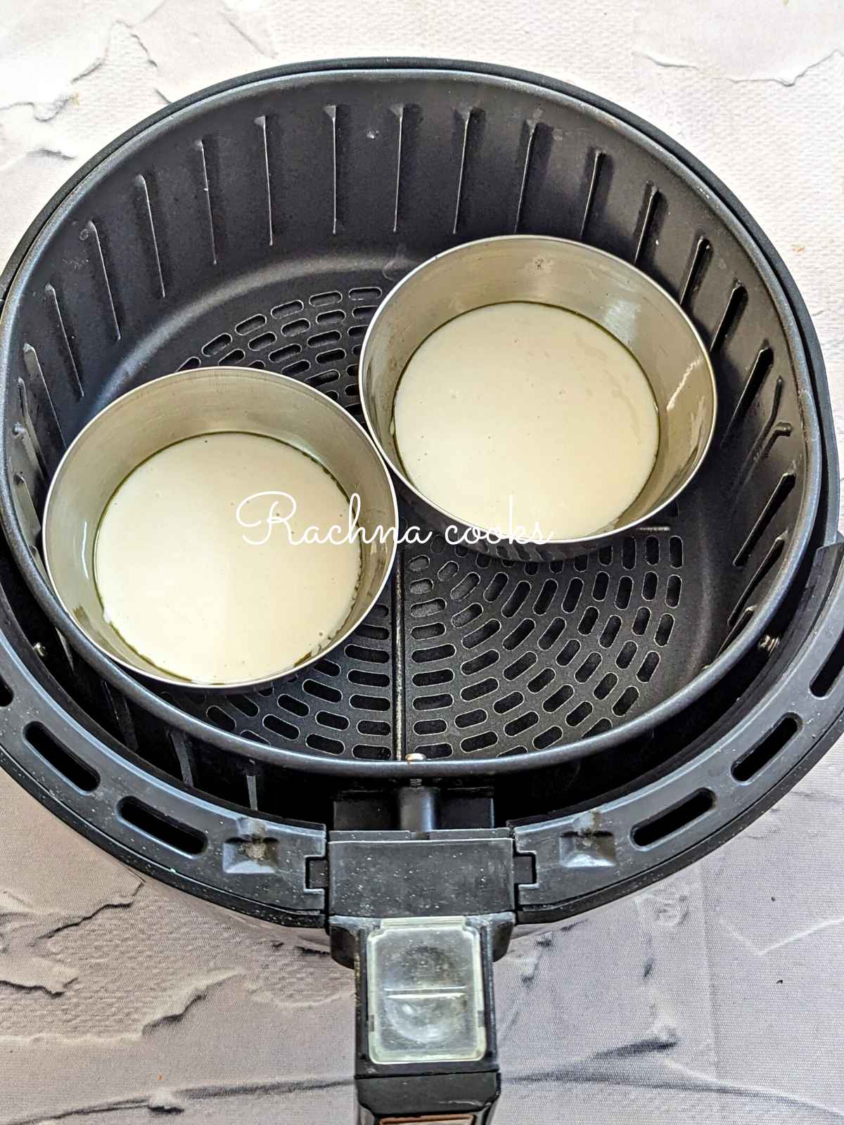 Pancake batter poured in two metal moulds placed in air fryer basket for air frying.