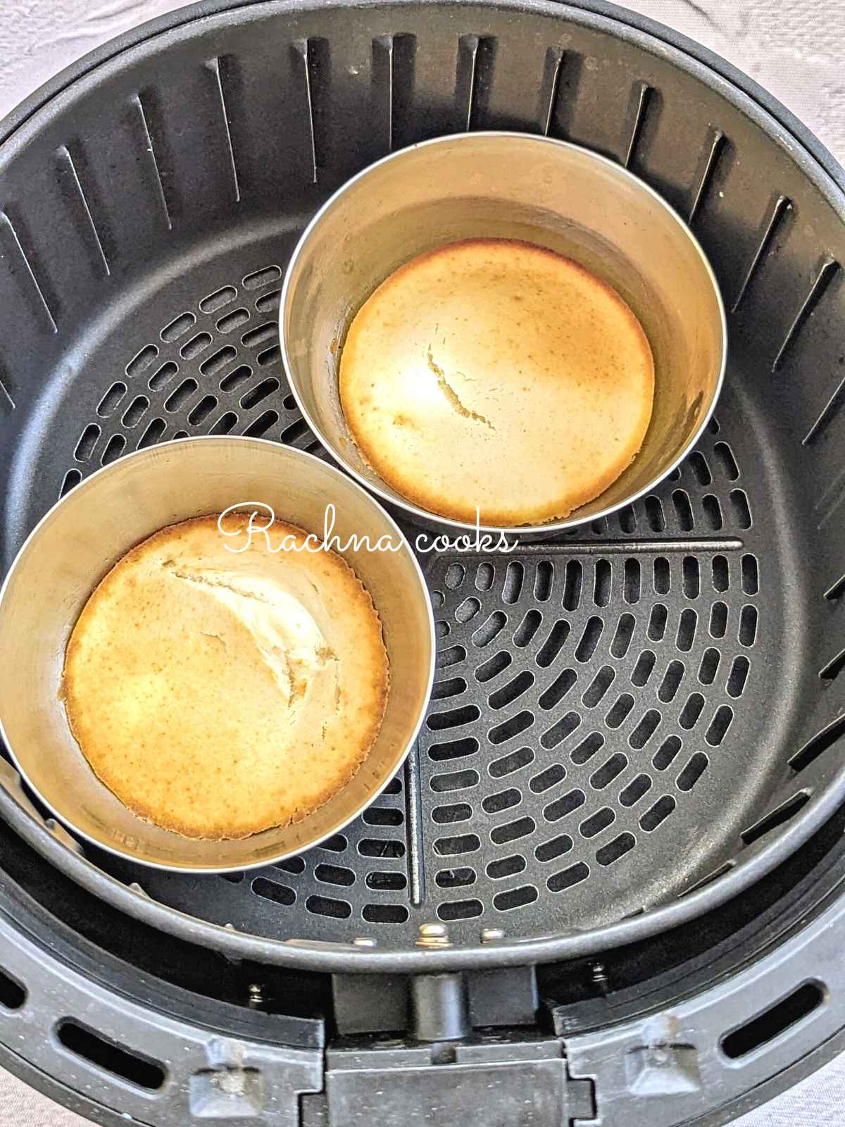Two pancakes cooked in metal moulds placed in air fryer basket.