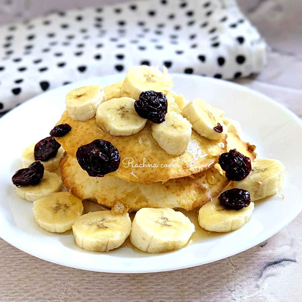 Two air fryer pancakes with a drizzle of maple syrup, cut bananas and cherries.