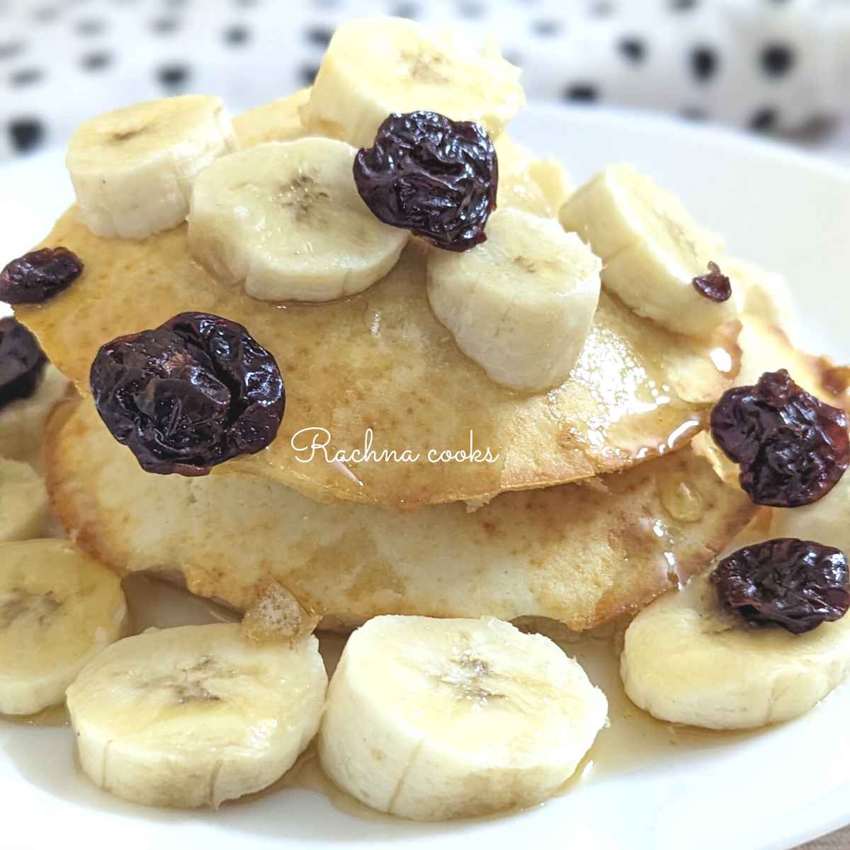 Two air fryer pancakes with a drizzle of maple syrup, cut bananas and cherries.