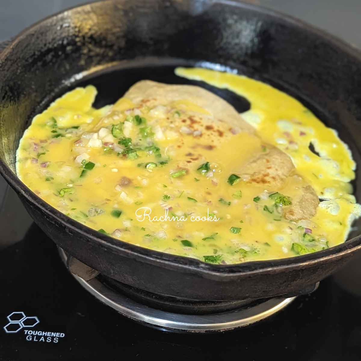 Omelette mixture on top of paratha in a skillet