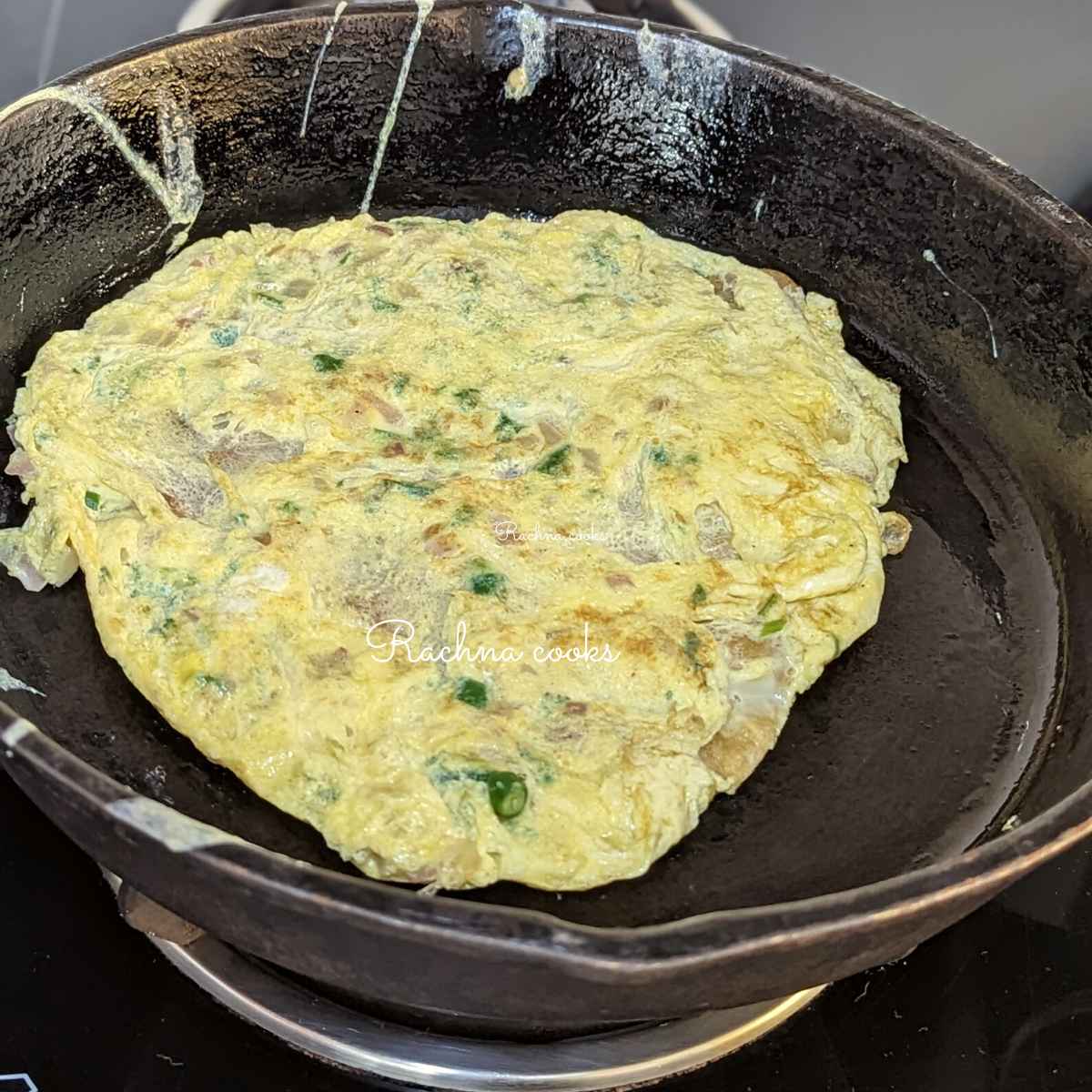 Cooked omelette on top of a cooked paratha in a skillet.