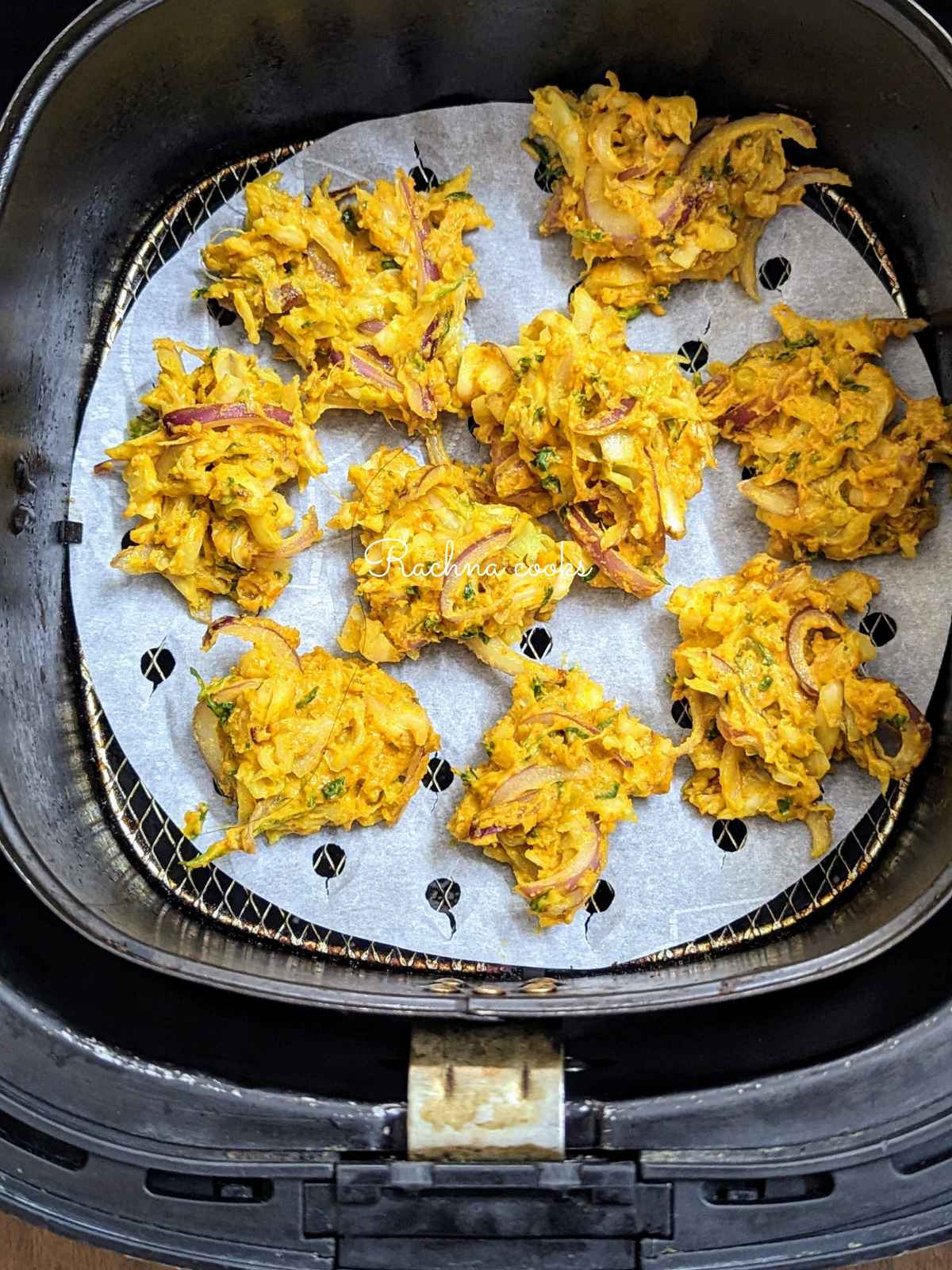 cabbage pakoda placed on perforated parchment paper in air fryer basket ready for air frying.