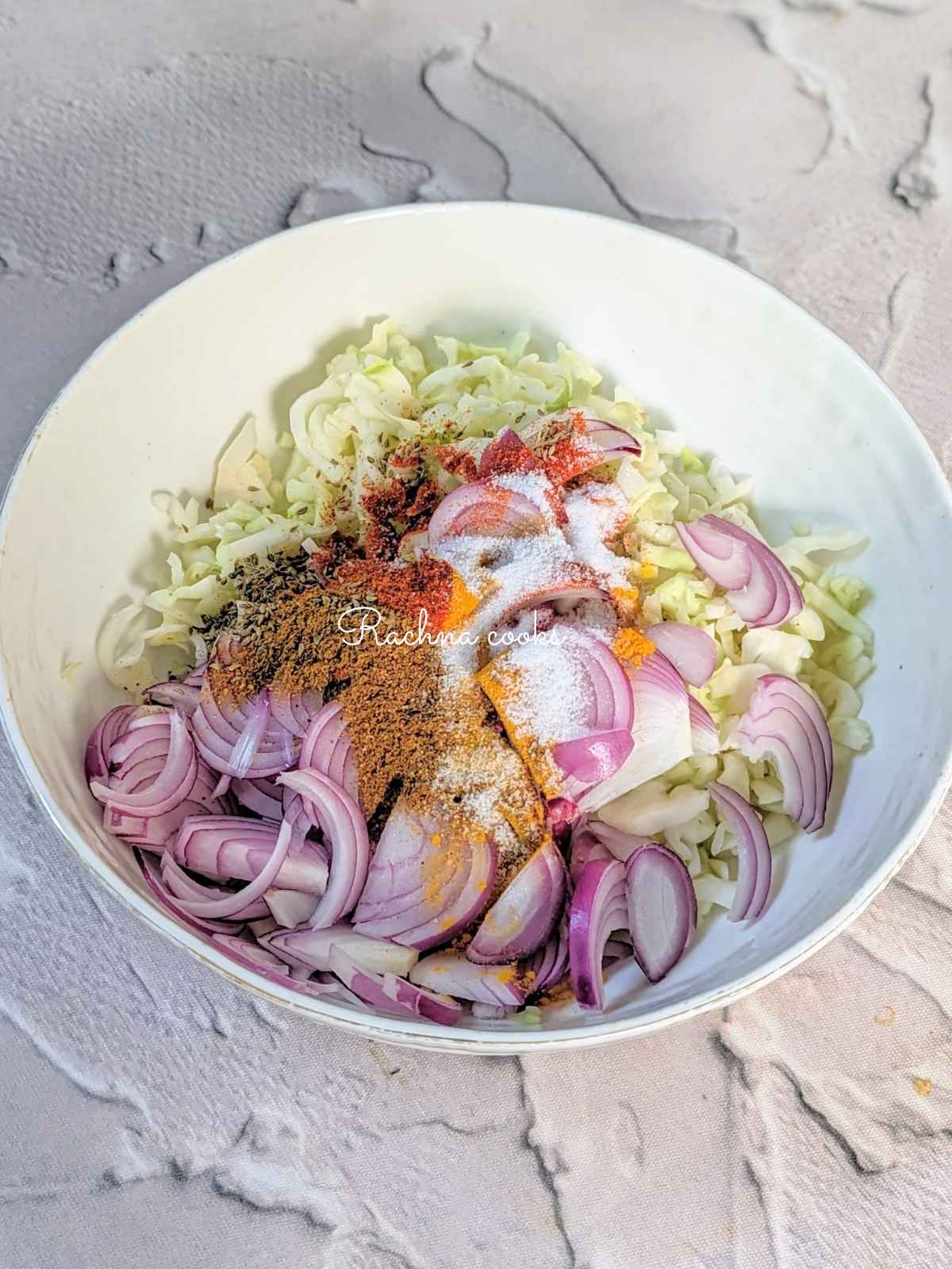 Shredded cabbage, sliced onion with spices and seasonings in a bowl.