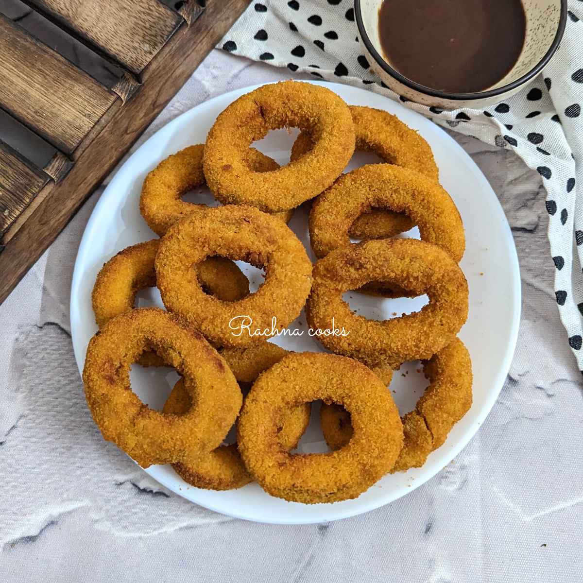 Frozen onion rings on a white plate with a dip in a bowl in the background