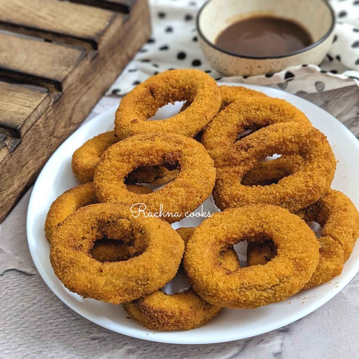 Frozen onion rings on a white plate with a dip in a bowl in the background