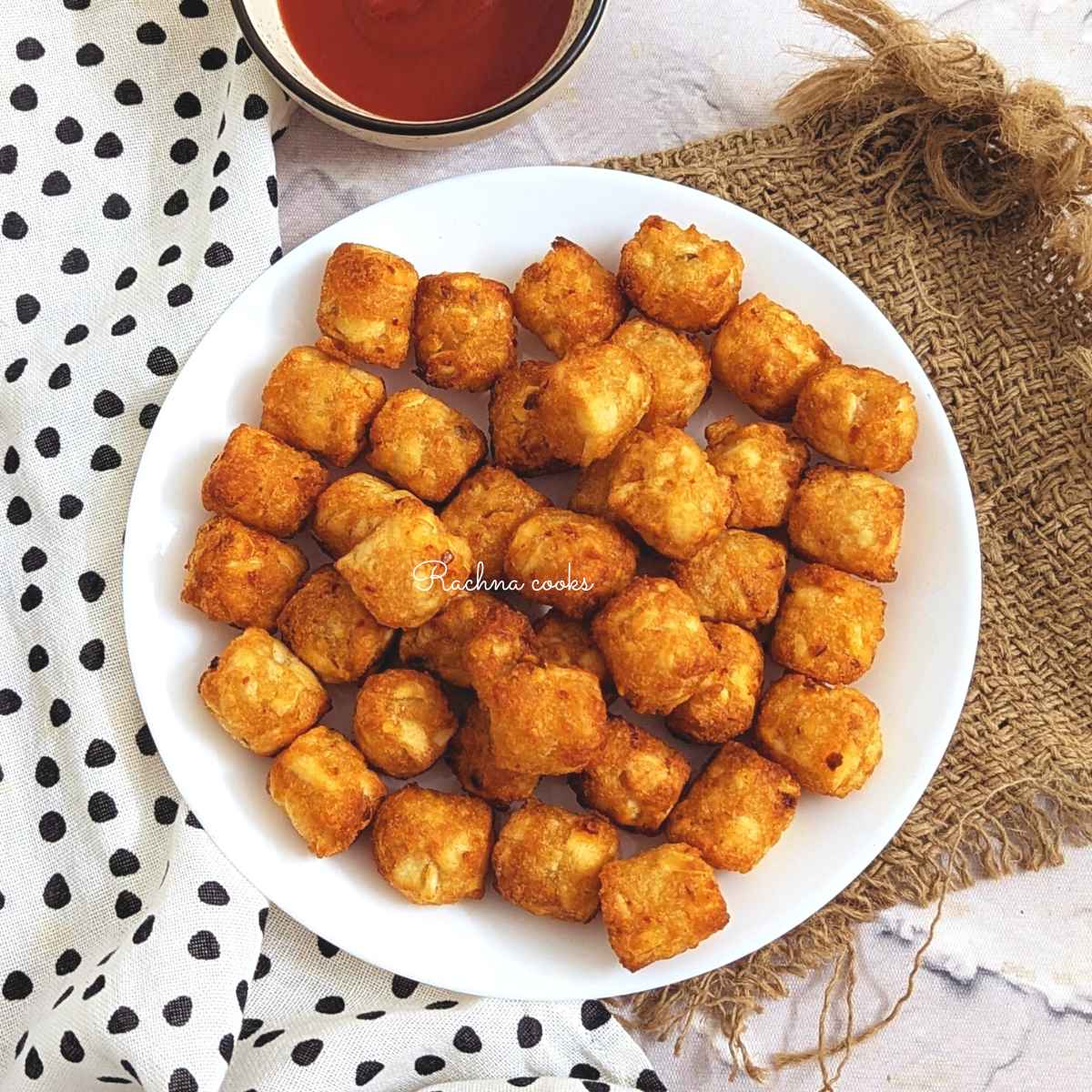 Golden tater tots served on a white plate.