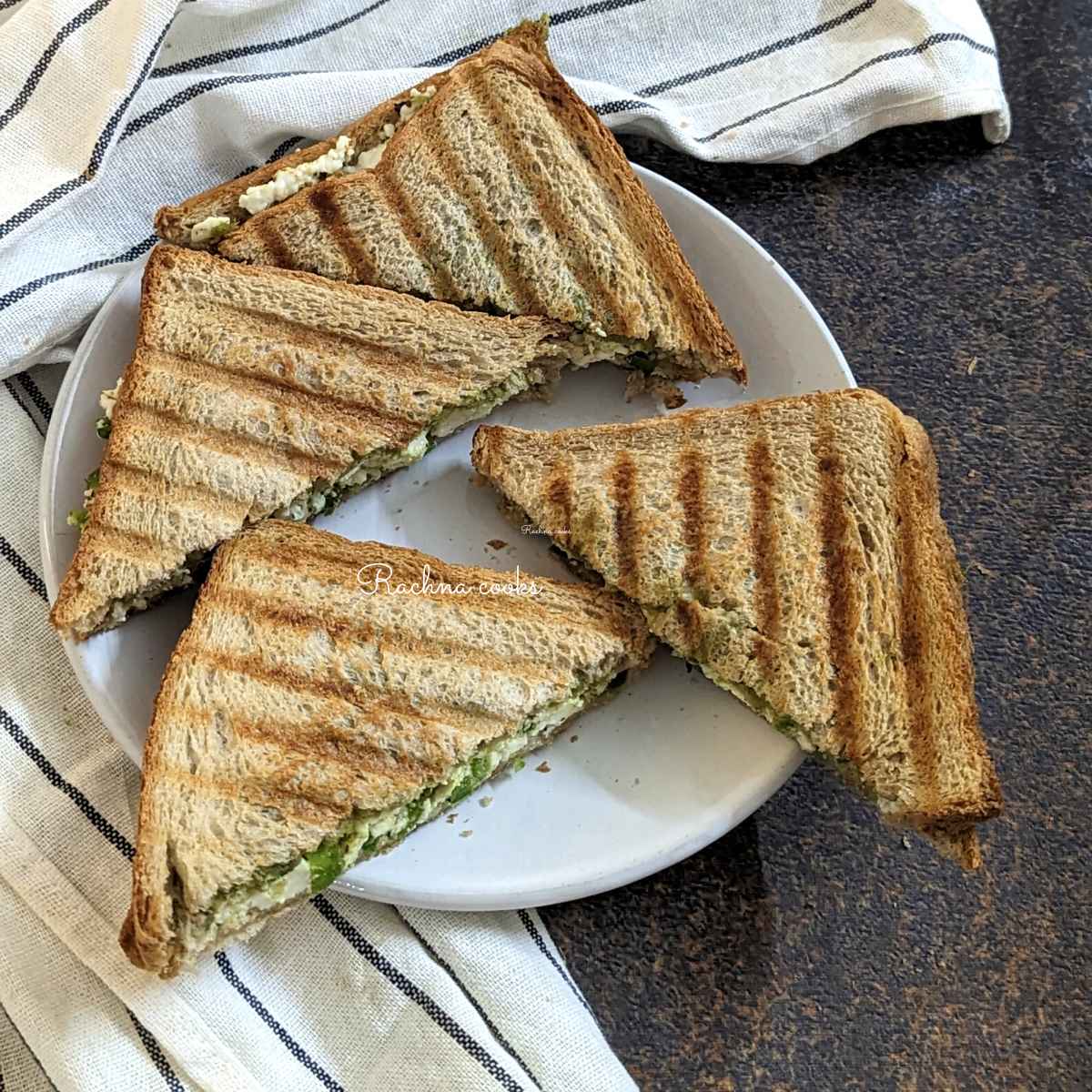 Two paneer sandwich halves cut into triangles and served on a white plate.