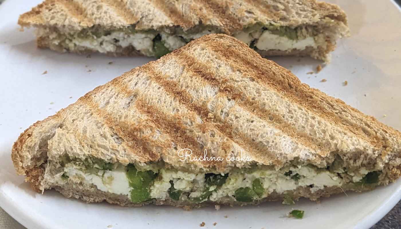 Two halves of paneer sandwich cut into triangles and served on a white plate.