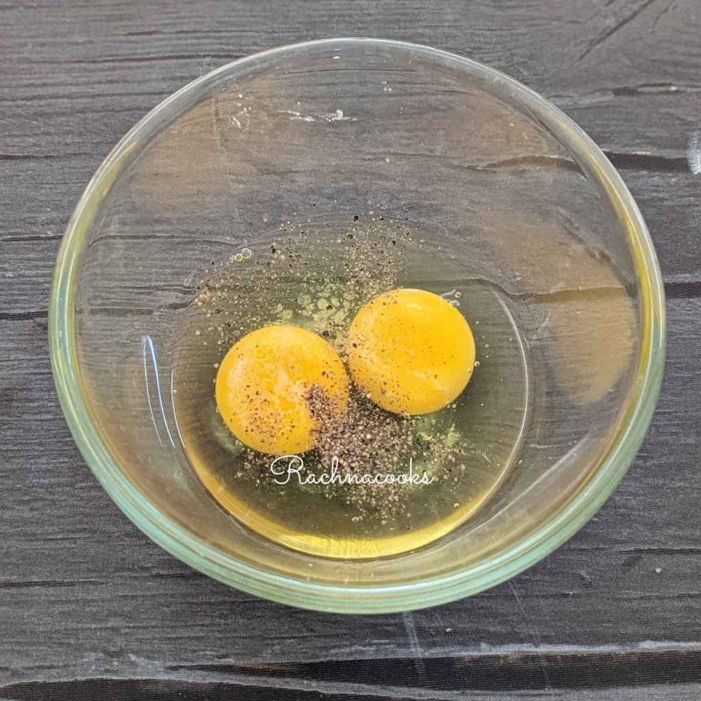 Two broken eggs with salt and pepper in a glass bowl