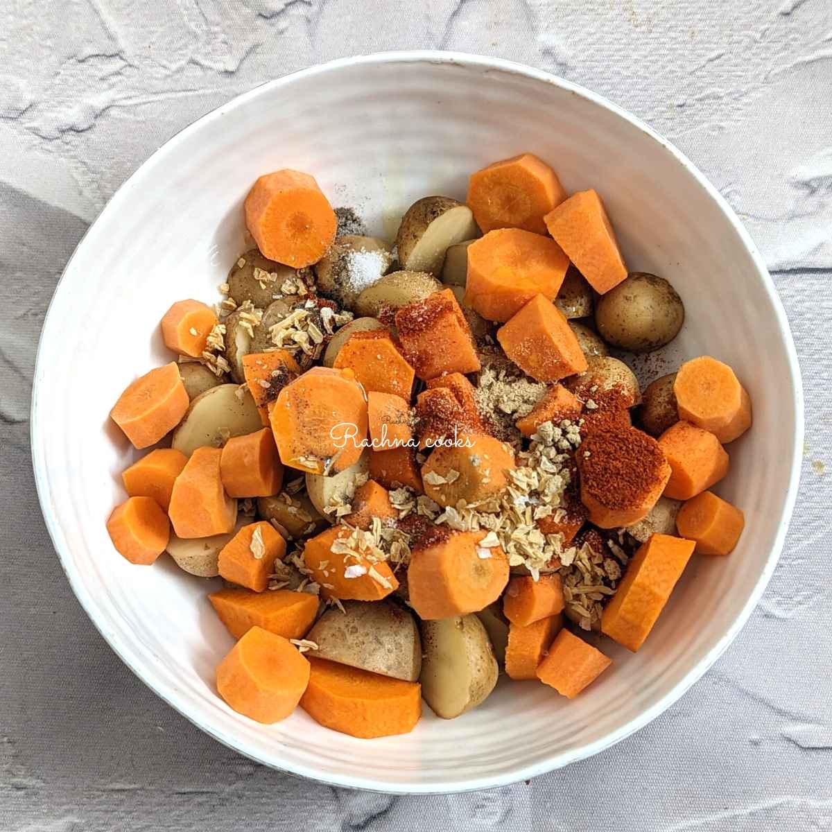 Chopped carrots and potatoes with seasonings and oil in a bowl