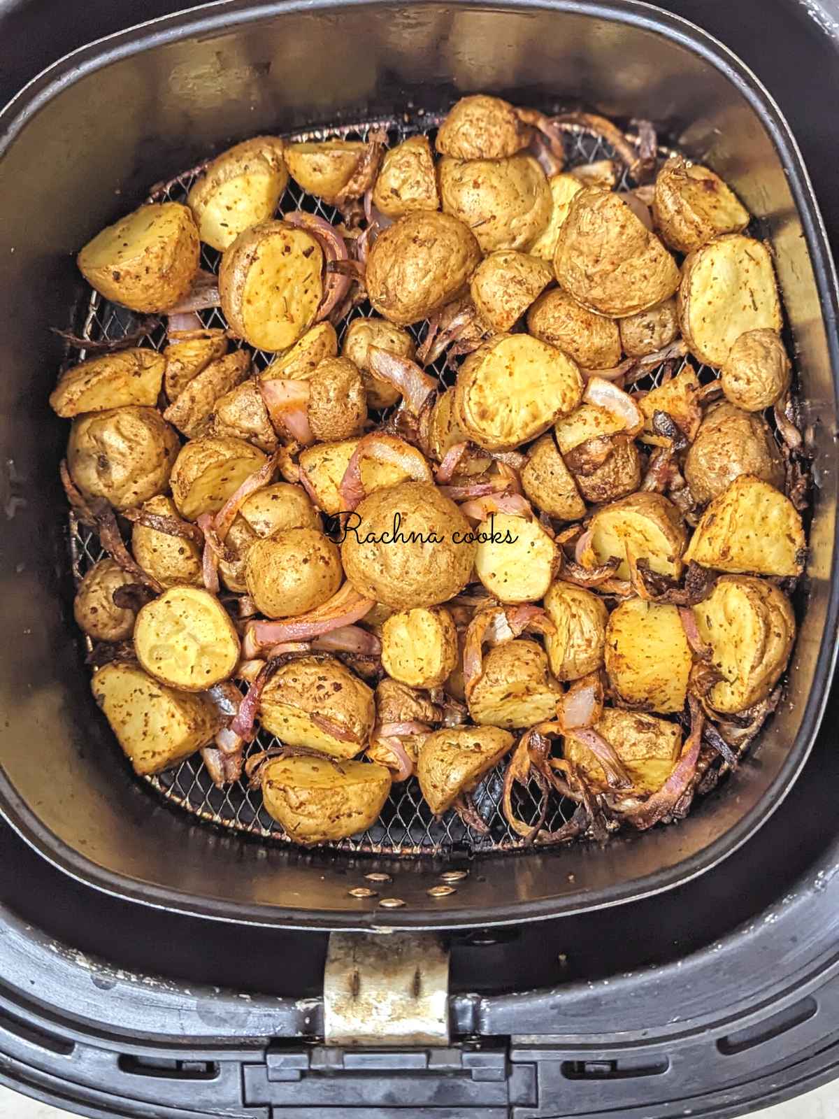 Roasted potatoes and onions in air fryer basket after air frying.