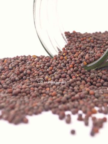 Black mustard seeds flowing out of a glass jar
