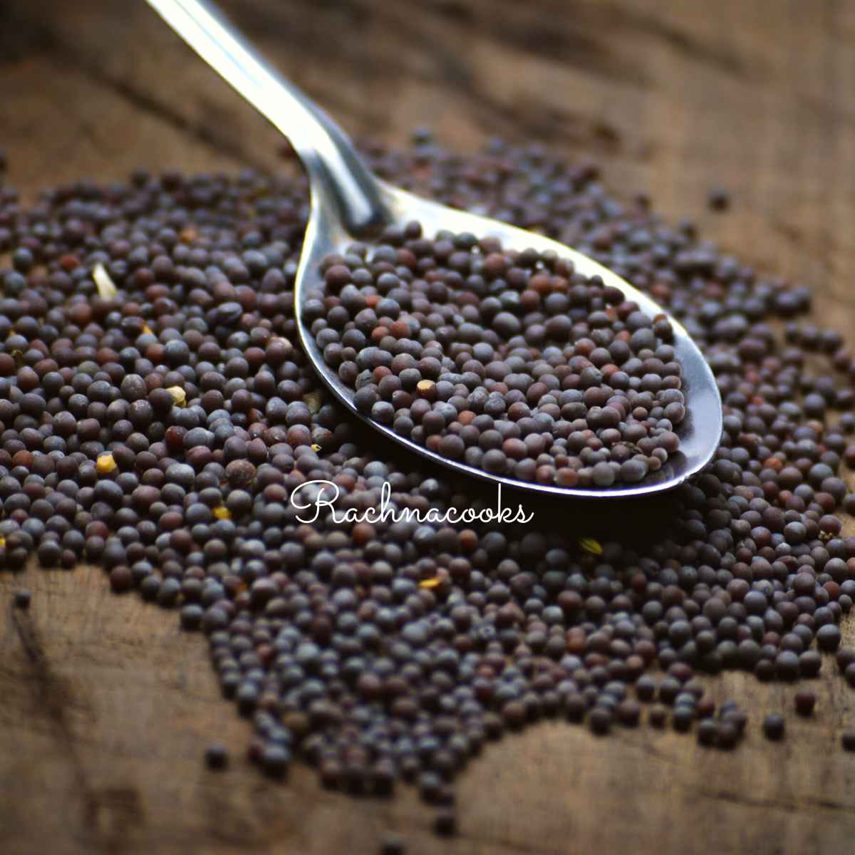 Black mustard seeds in a spoon with some scattered on a frame.