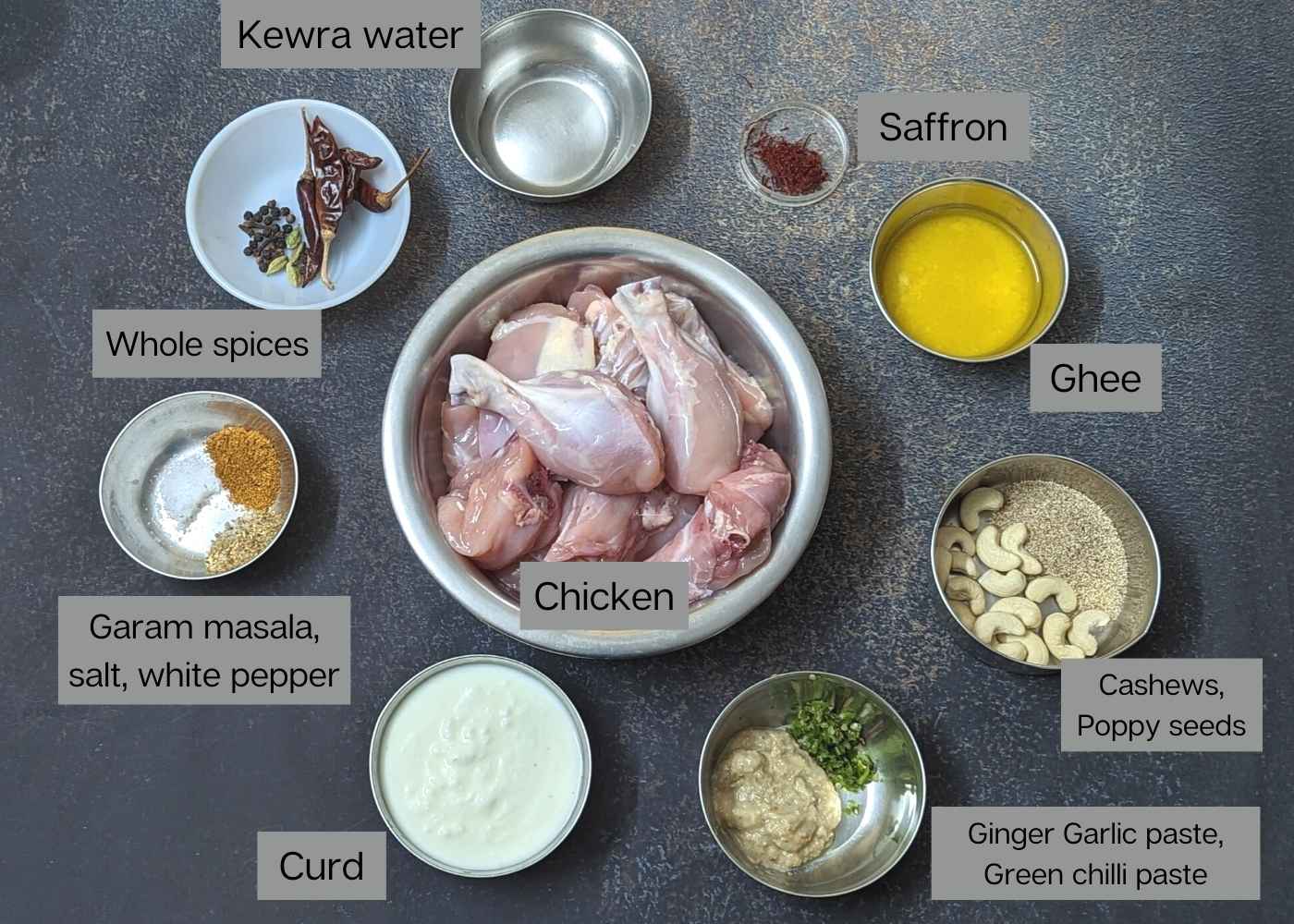 Ingredients for chicken rezala in a frame: bone-in chicken pieces, ghee, saffron, cashews, poppy seeds, whole spices, kewra water, spices, yogurt, ginger garlic paste and green chilli paste.