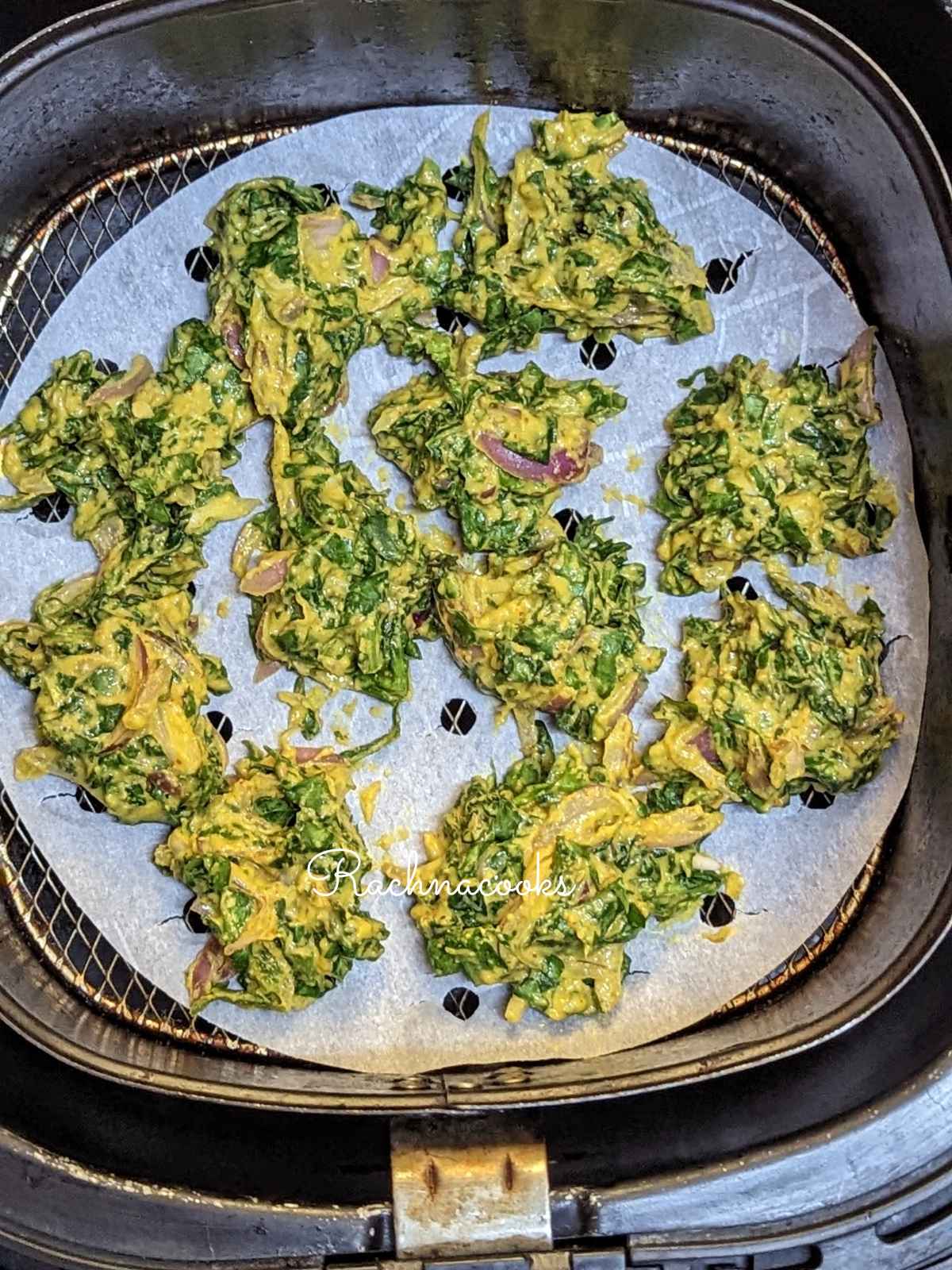 spinach pakoda placed on perforated parchment paper in air fryer.