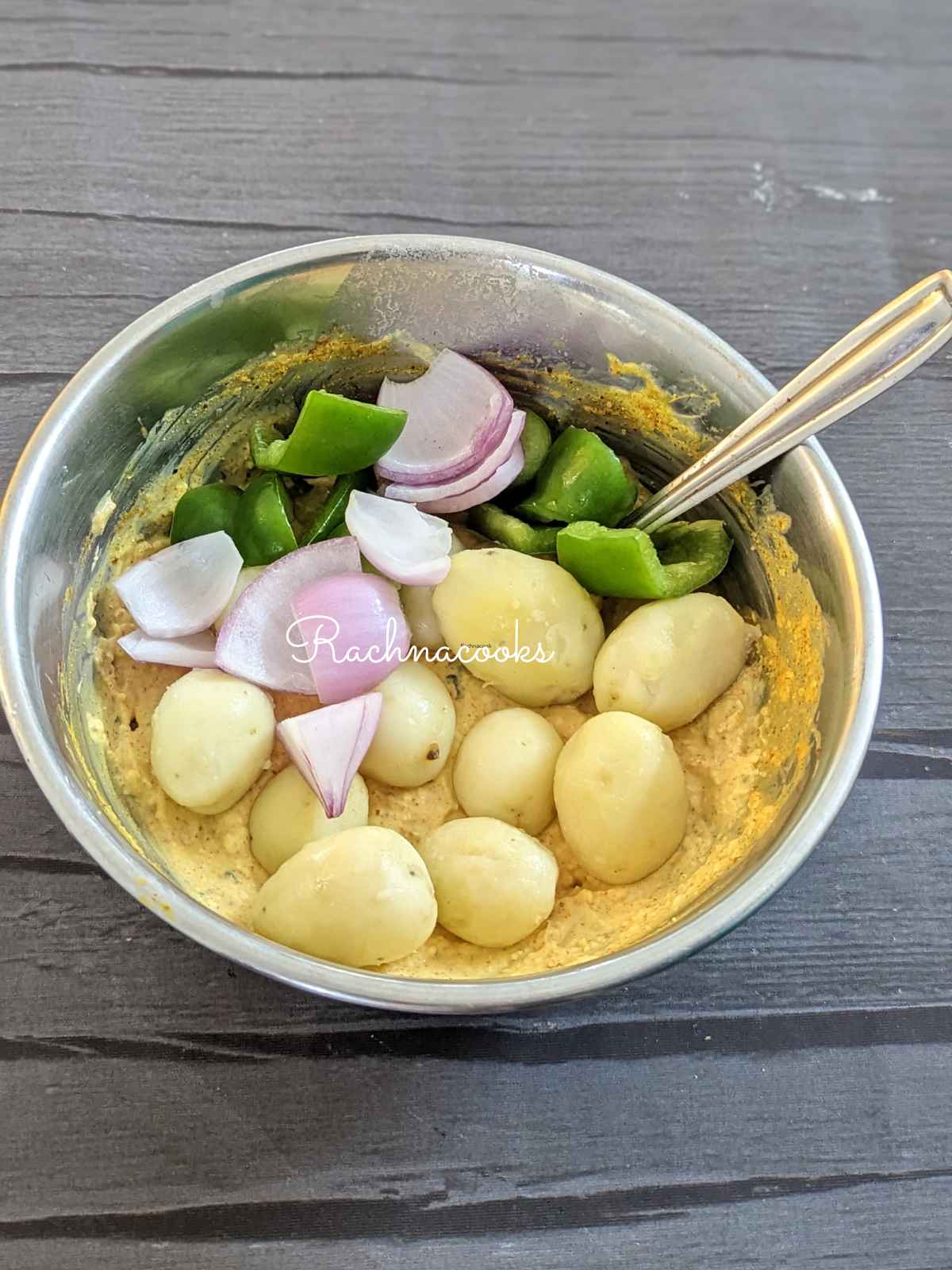 Baby potatoes, onion and green pepper being marinated in a thick marinade.