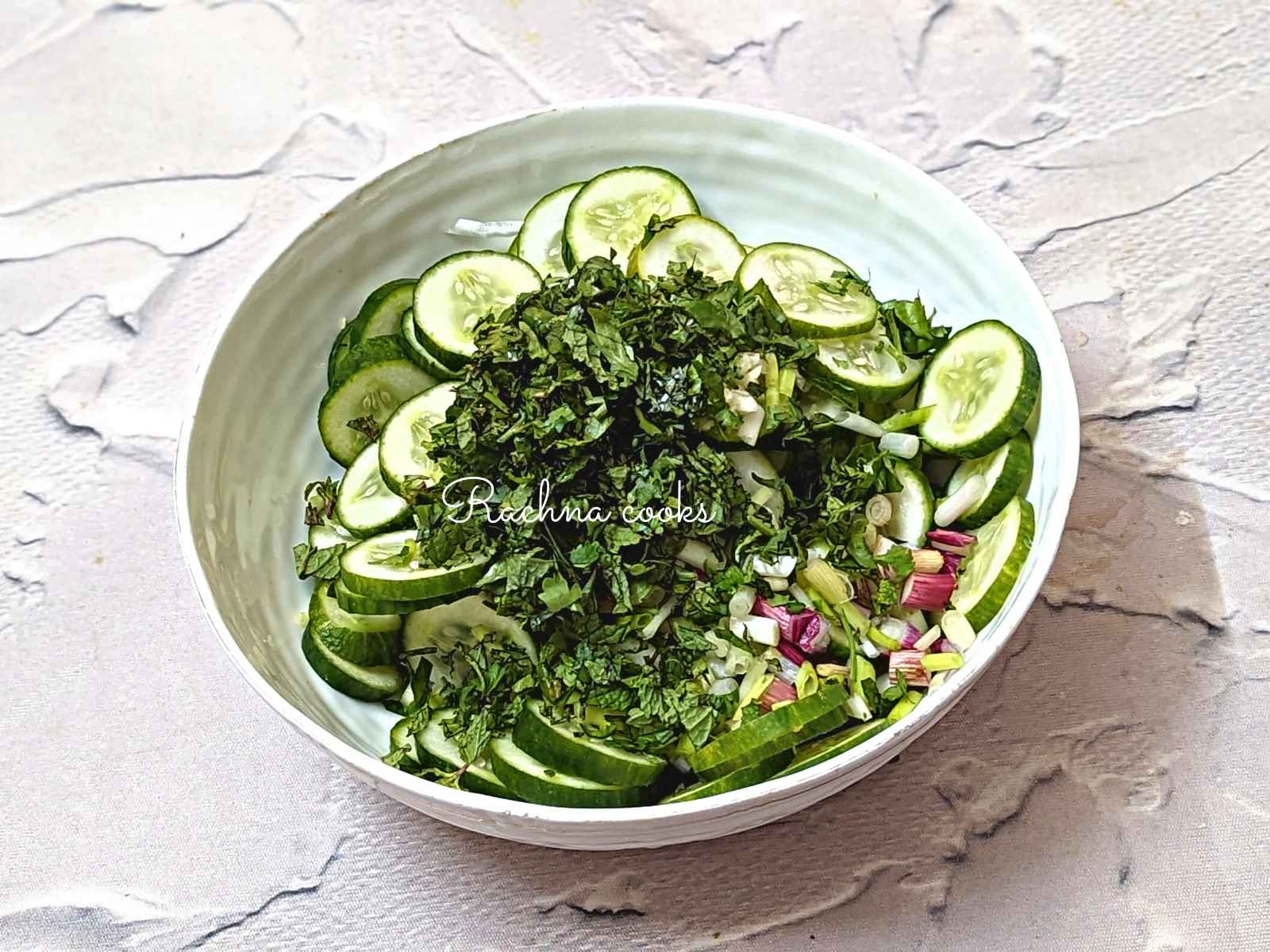 Sliced cucumber, scallions, mint and cilantro in a bowl.