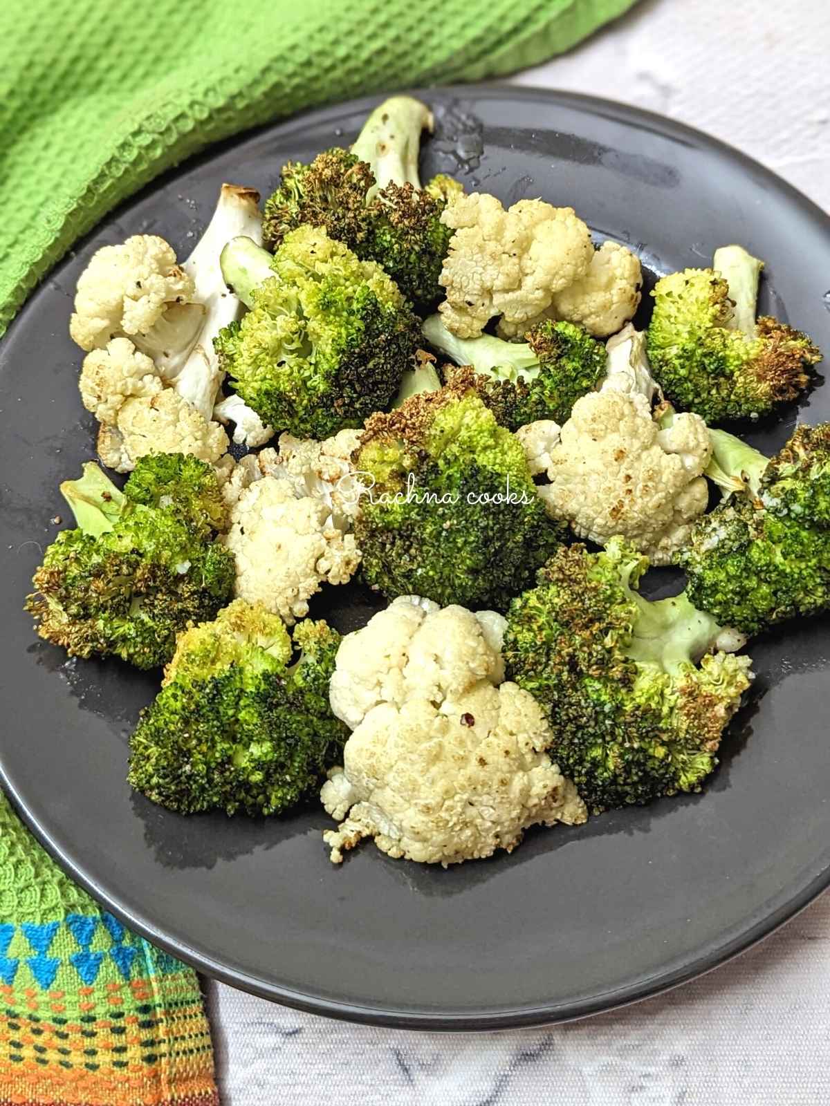 Charred air fried broccoli and cauliflower florets served on a black plate.