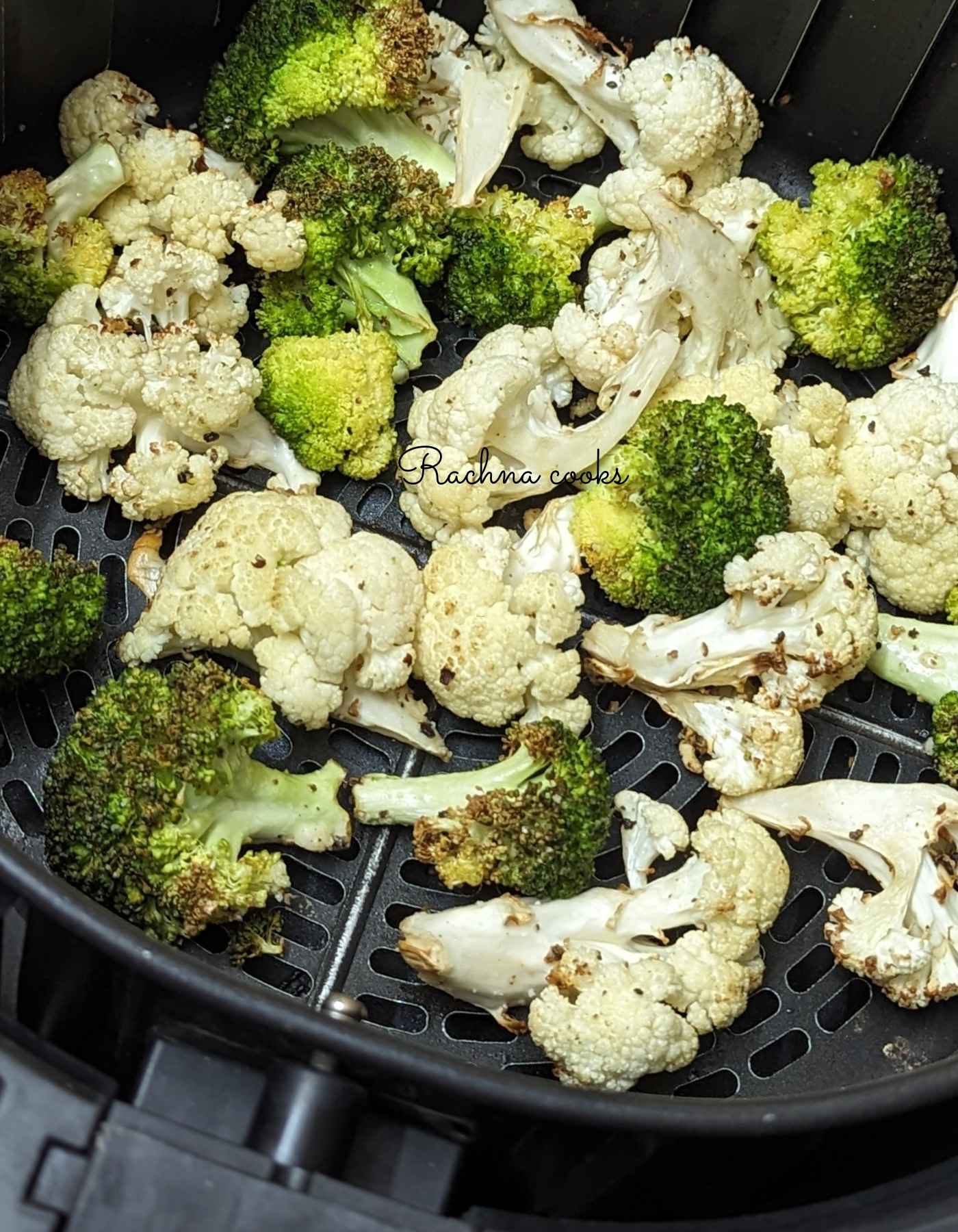 Charred cauliflower and broccoli florets in air fryer basket after air frying.