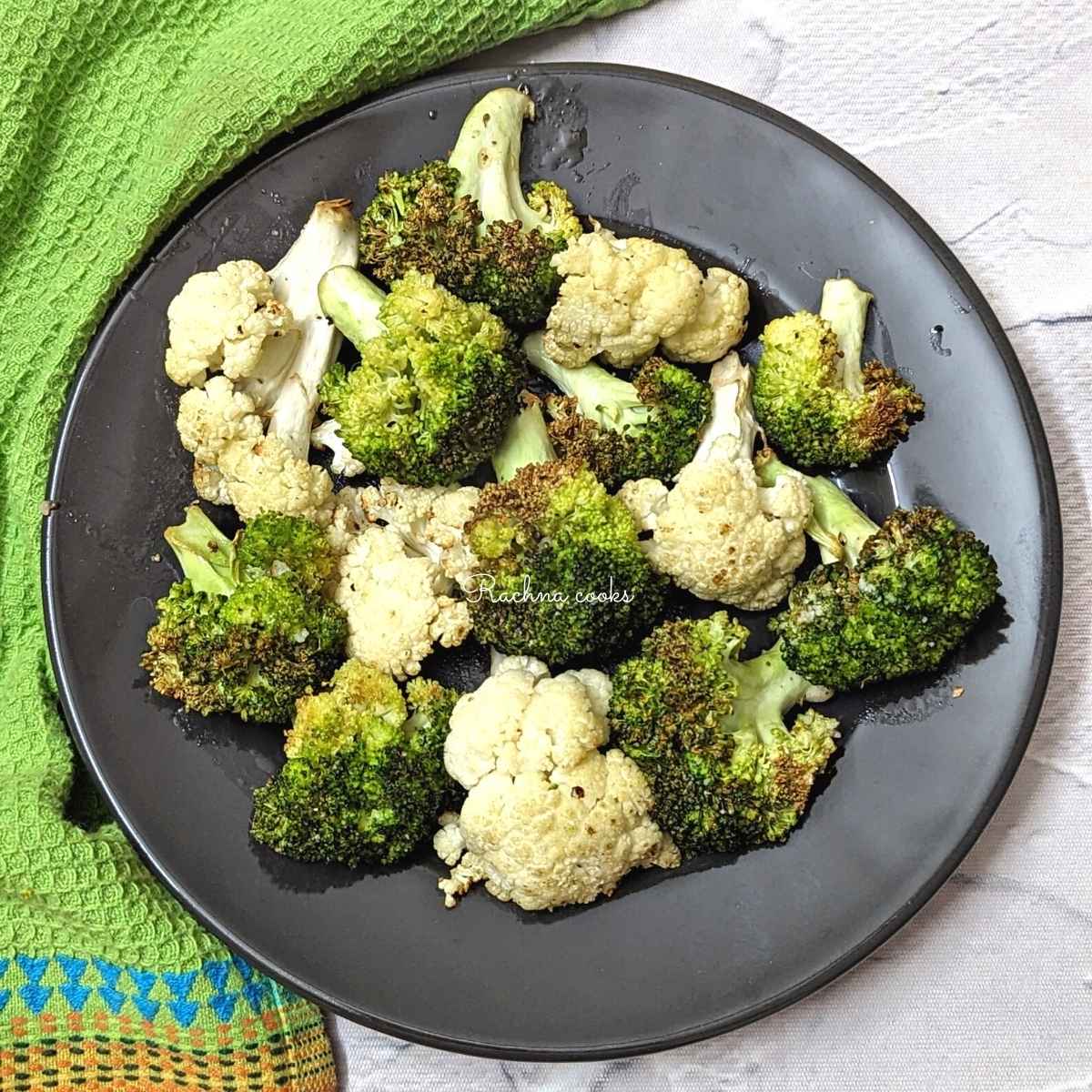 Charred air fried broccoli and cauliflower florets served on a black plate.