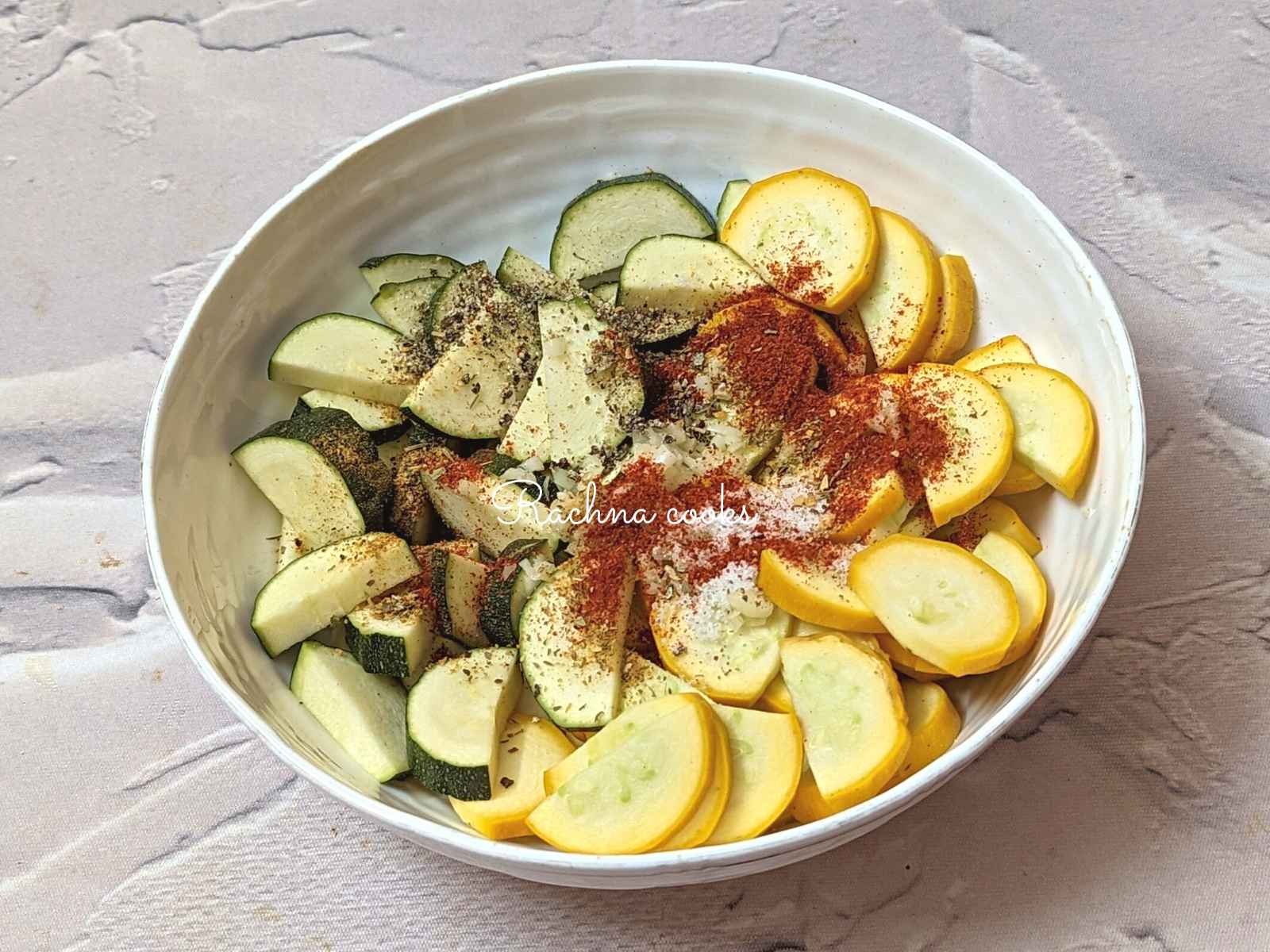 Sliced zucchini and squash with seasonings and oil in a bowl.