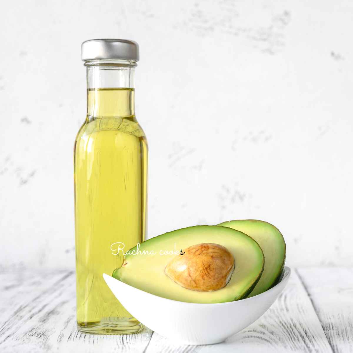 A bottle of avocado oil with cut avocado in the background.