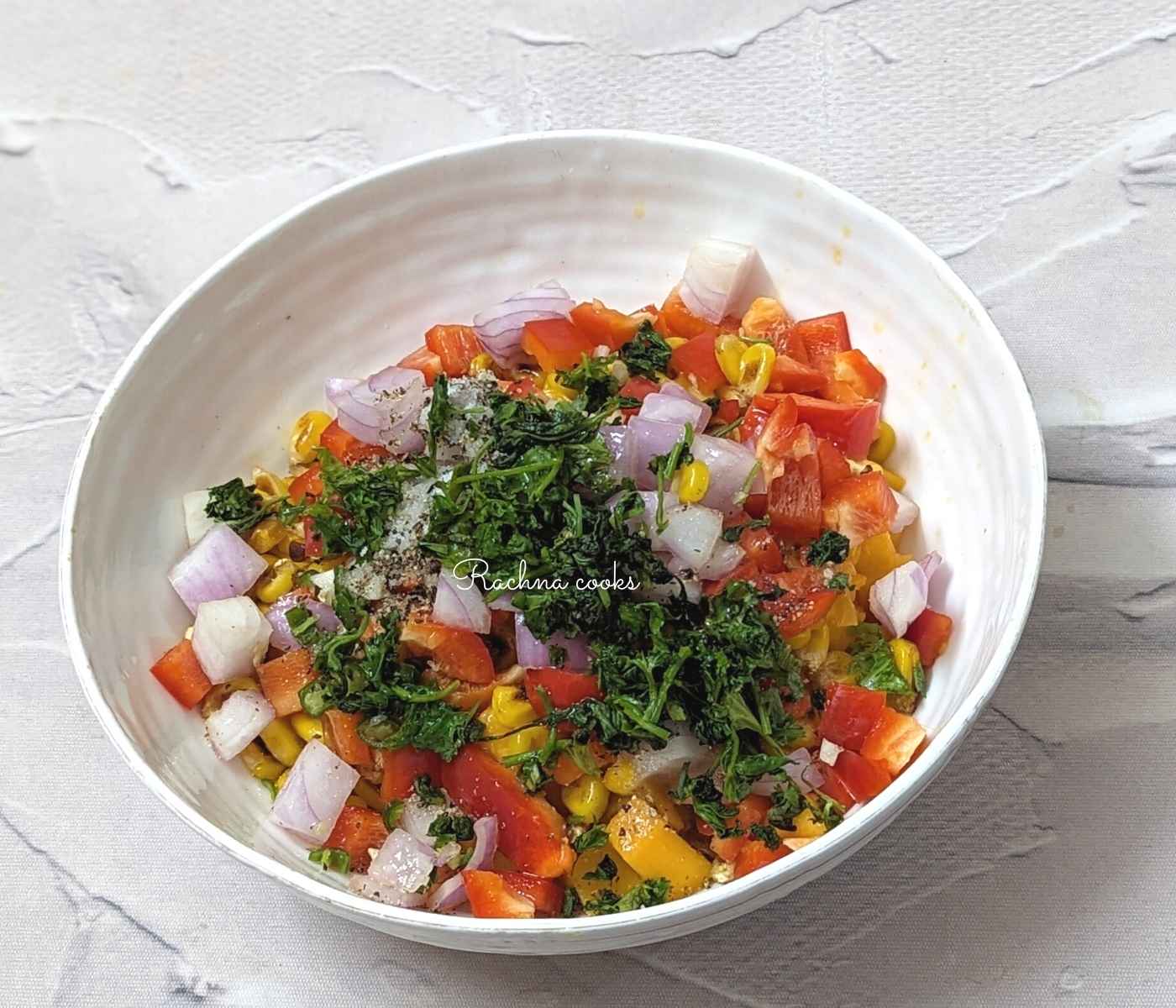 Cilantro leaves added to mango, corn, pepper, onion, chilli and seasonings in a bowl