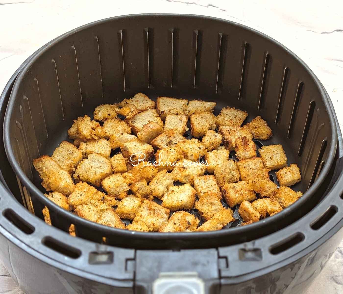 seasoned bread cubes laid out in air fryer basket ready for air frying.