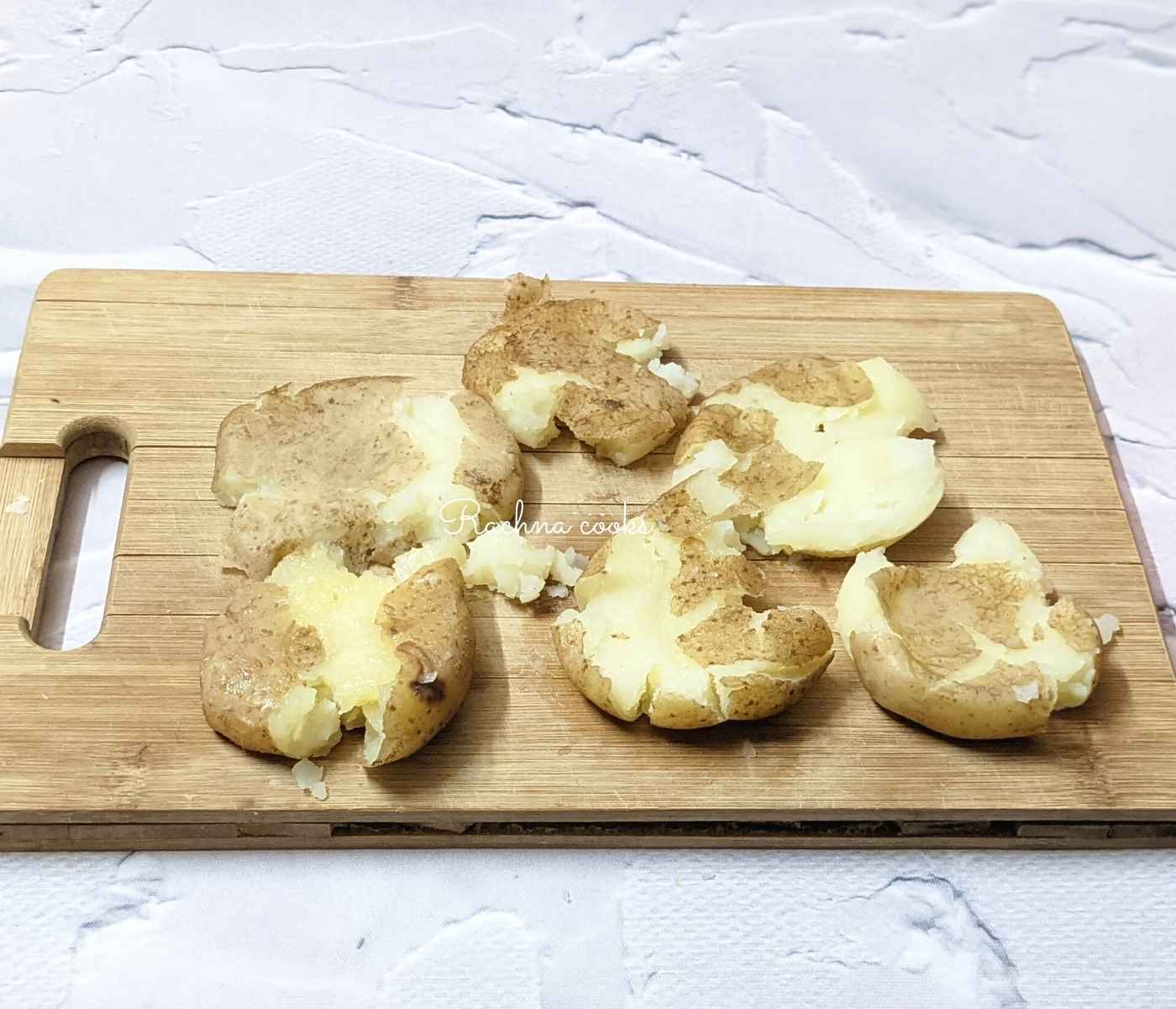 Boiled potatoes smashed with a glass on a chopping board.