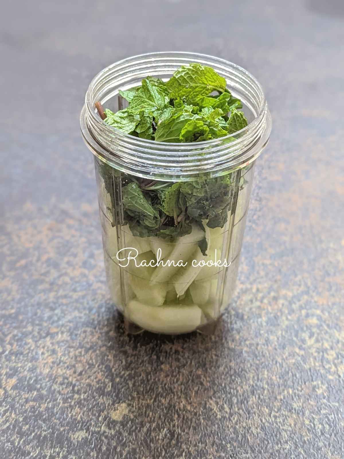 Blender jar with cucumber pieces and mint leaves