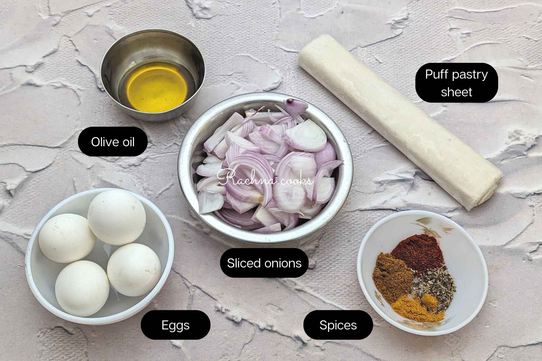 Ingredients for making air fryer egg puffs including sliced onions, boiled eggs, puff pastry sheets, spices and olive oil