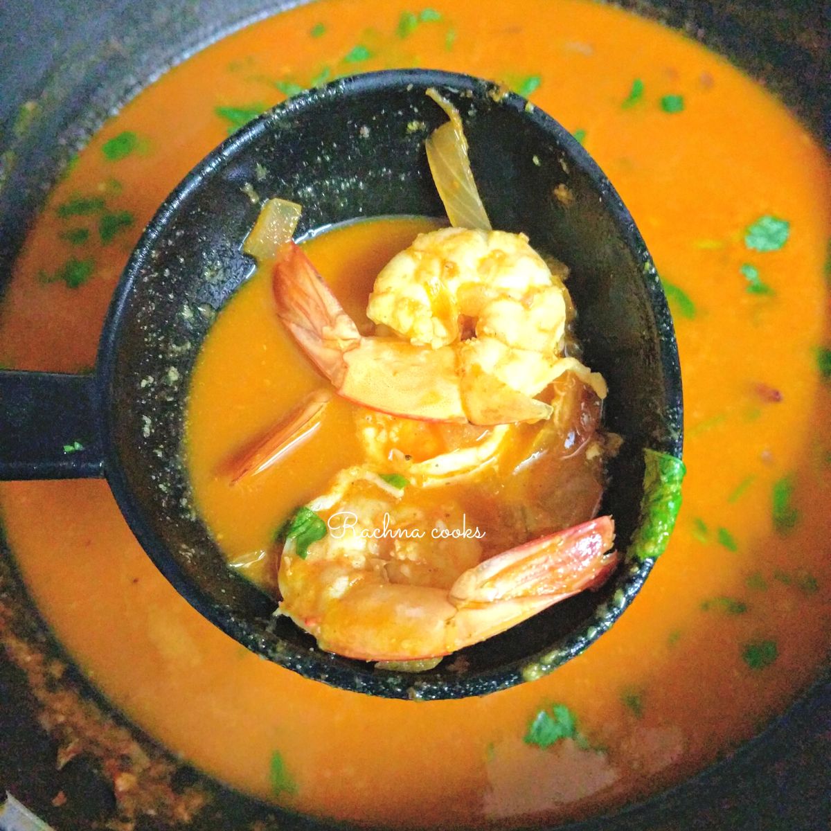 Prawn curry held up in ladle with two prawns visible