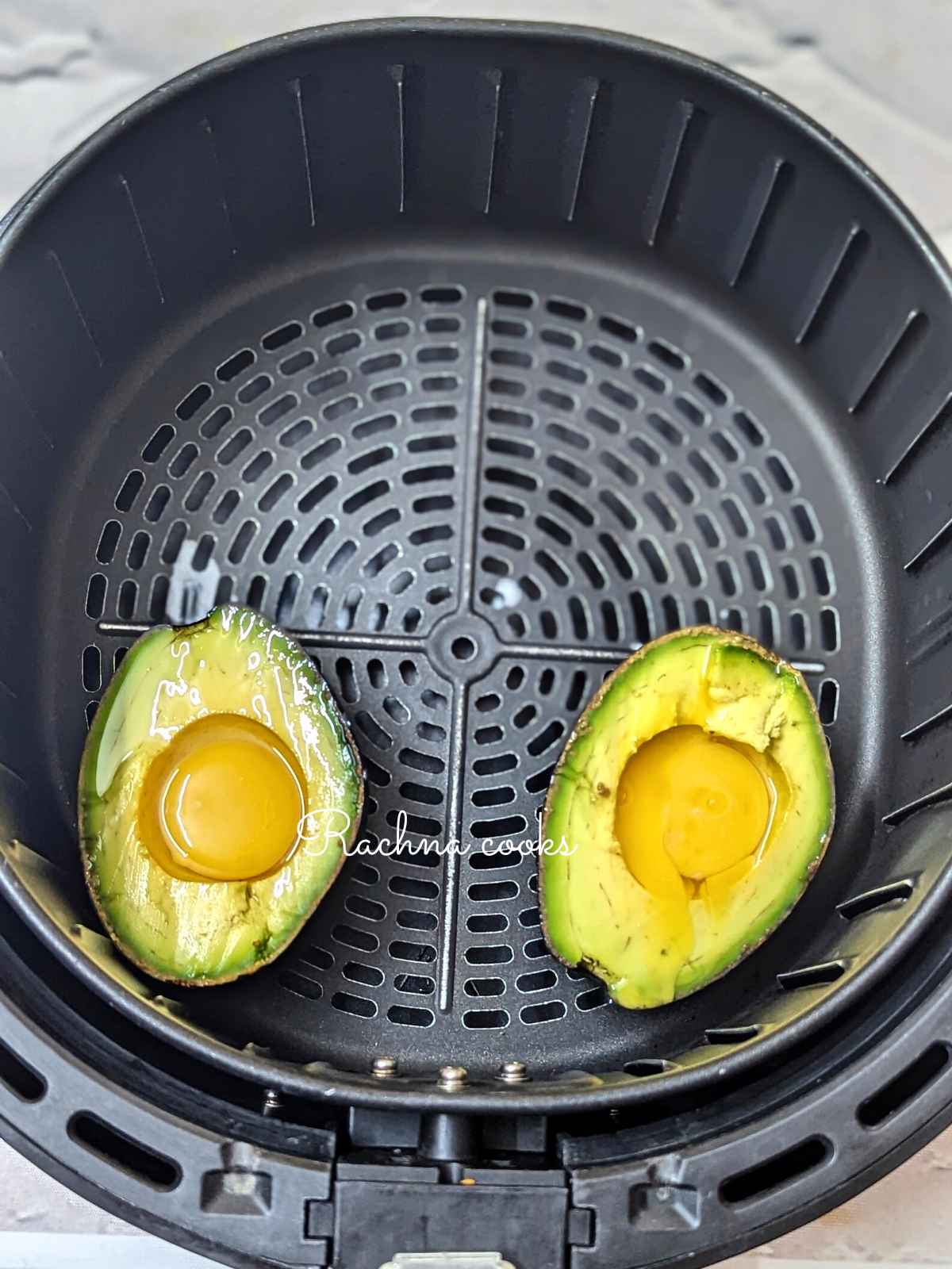 2 avocado eggs ready for air frying in air fryer basket.