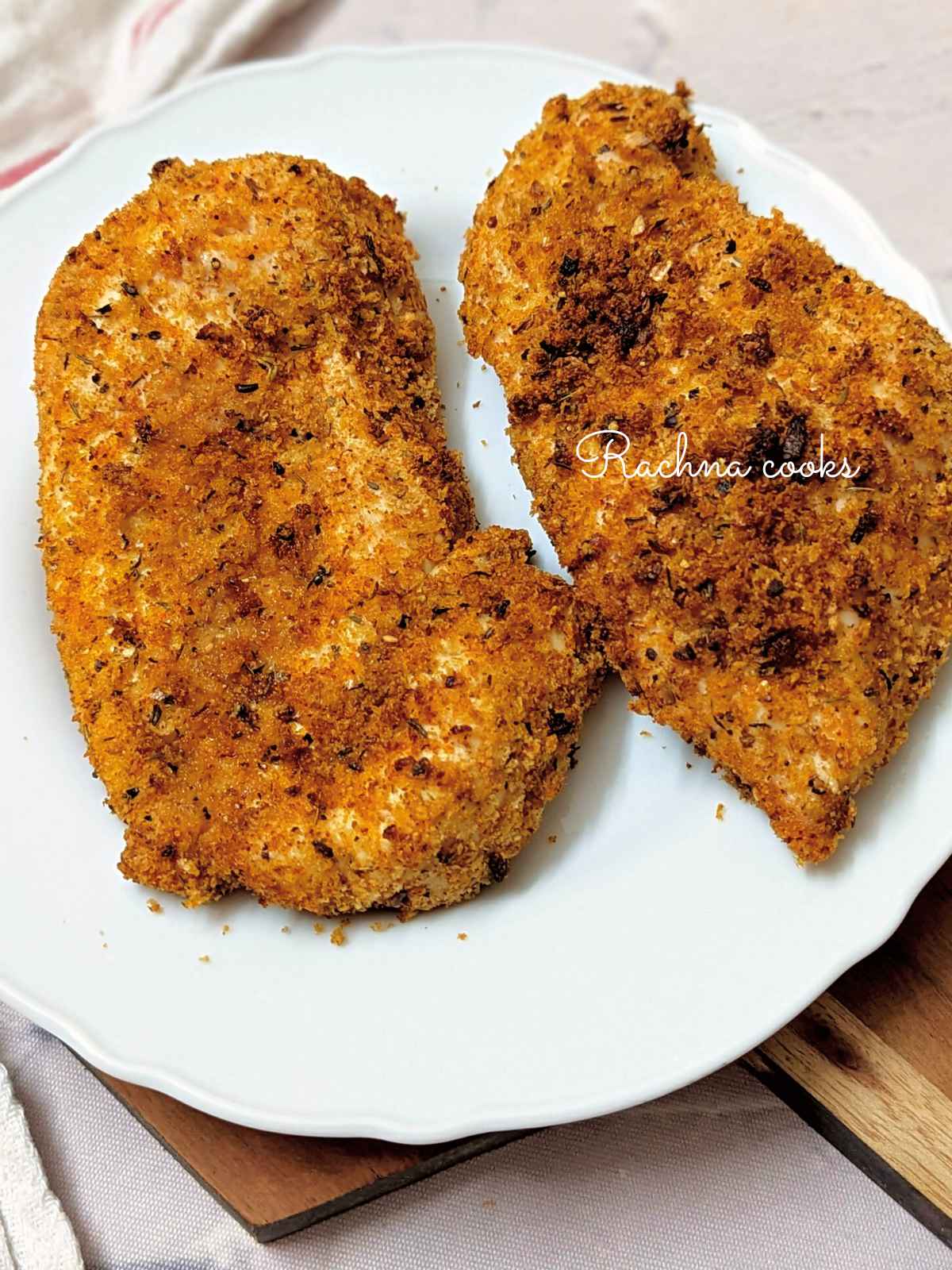 two shake and bake chicken breasts after air frying kept on a white plate.