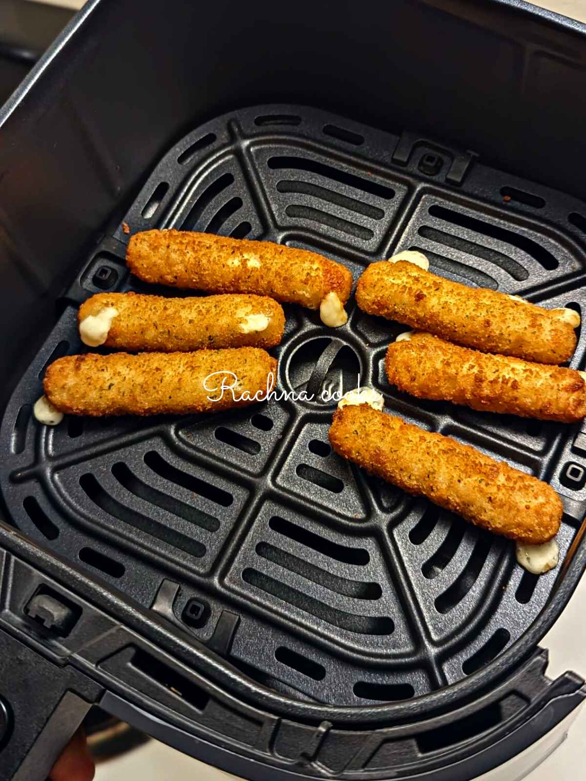 Crispy golden mozzarella sticks after air frying in air fryer basket.