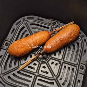Two air fried corn dogs served in air fryer basket.