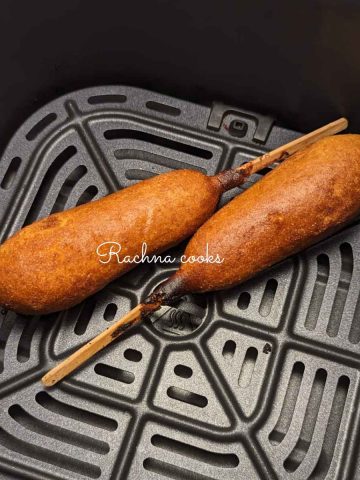 Two air fried corn dogs served in air fryer basket.