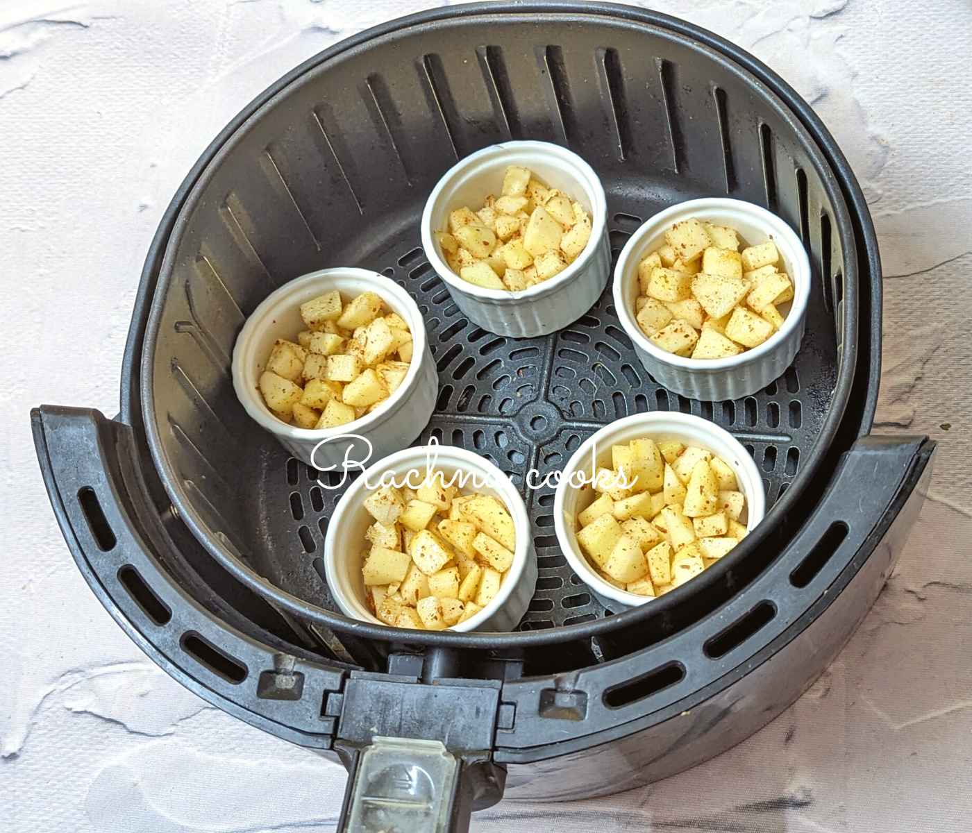 5 ramekins with spiced apple cubes in air fryer basket